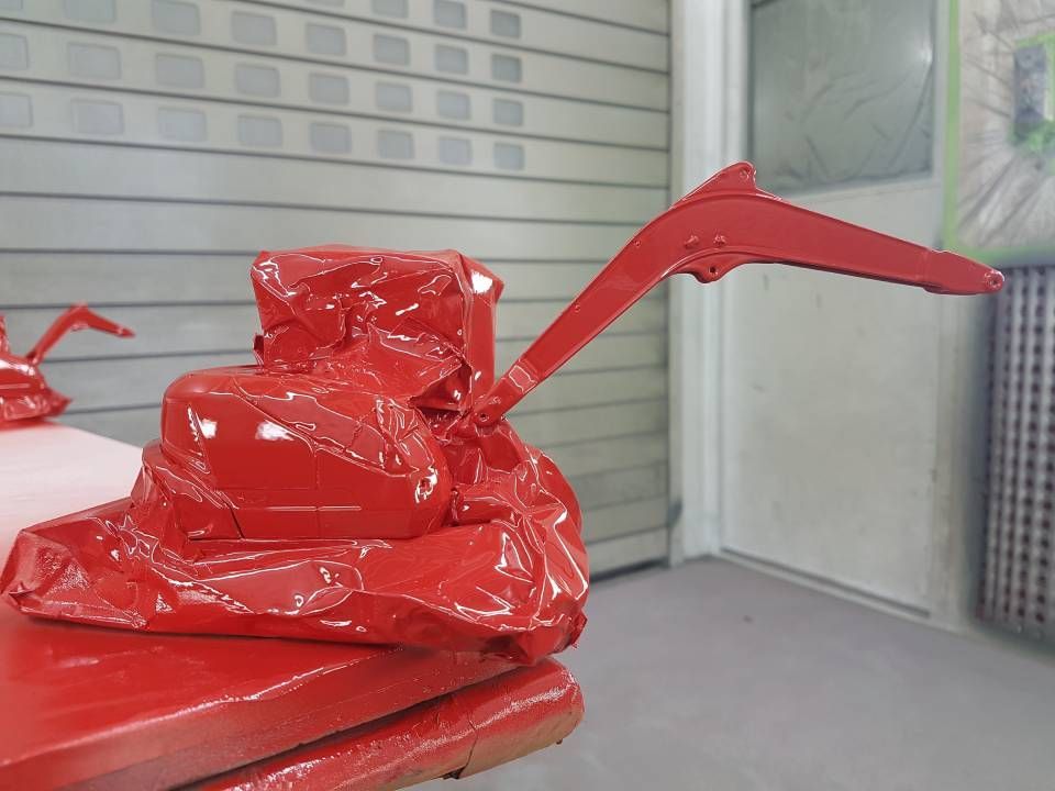 Eine rot lackierte Maschine mit langem Arm, vermutlich frisch lackiert, in einer Werkstatt.