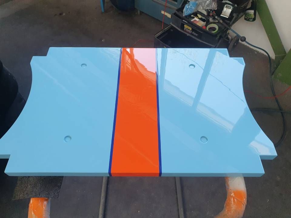 Tischplatte mit blauer und oranger Lackierung, abgerundeten Kanten und reflektierender Oberfläche.