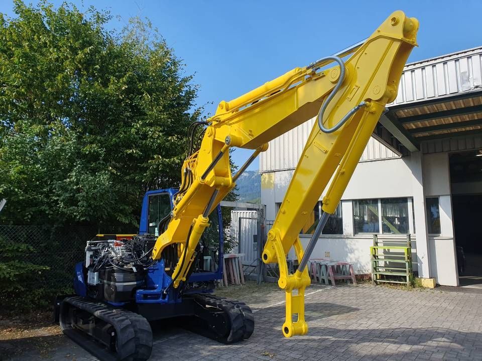 Ein gelb-blauer Bagger parkt an einem sonnigen Tag vor einem Gebäude.