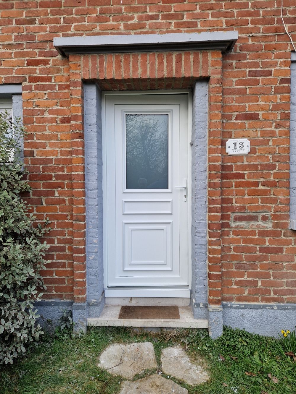 Porte d'entrée vitrée sur un mur de briques rouges