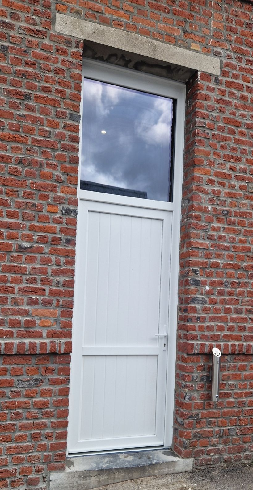 Vue de profil sur une porte d'entrée en pvc blanc avec un vitre sur le haut