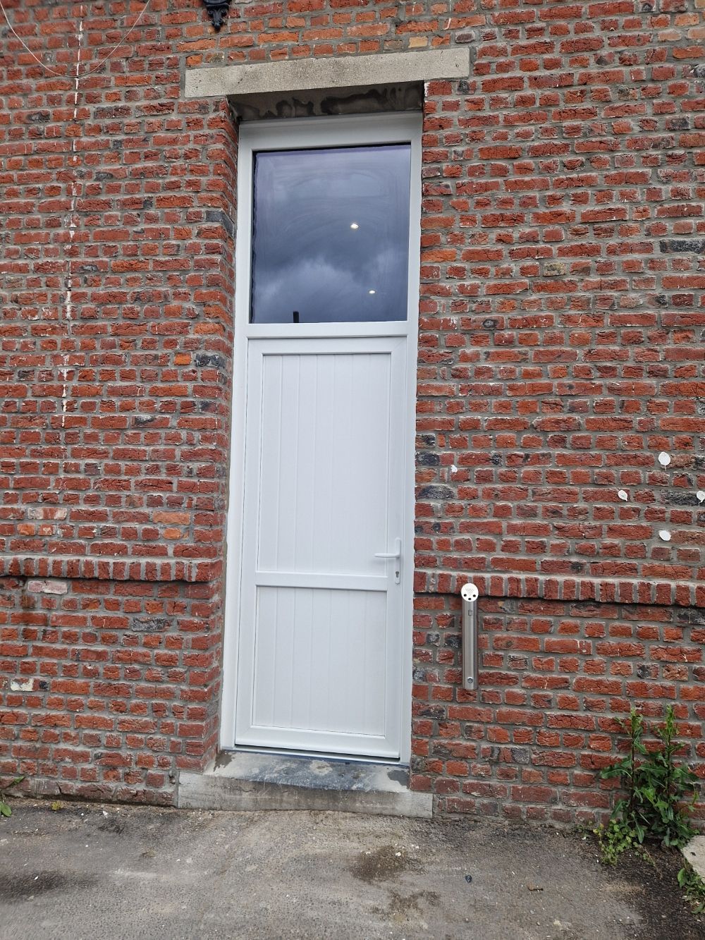 Porte d'entrée en pvc blanc avec un vitre sur le haut sur un mur en briques rouges
