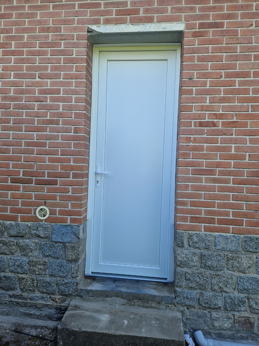 Porte d'entrée en pvc blanc sur un mur en briques rouges