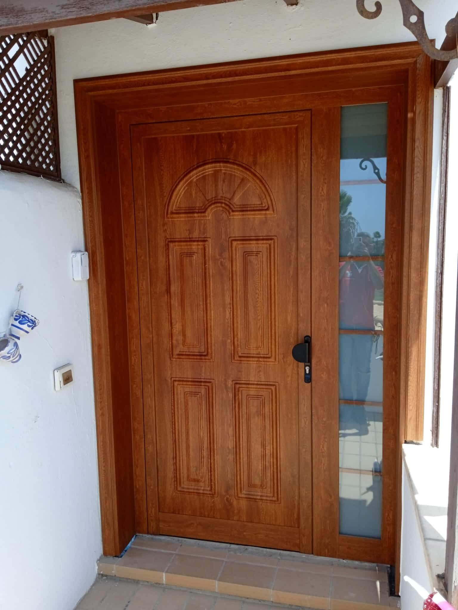 Puerta de entrada de madera con panel de vidrio, marco marrón, en un porche.