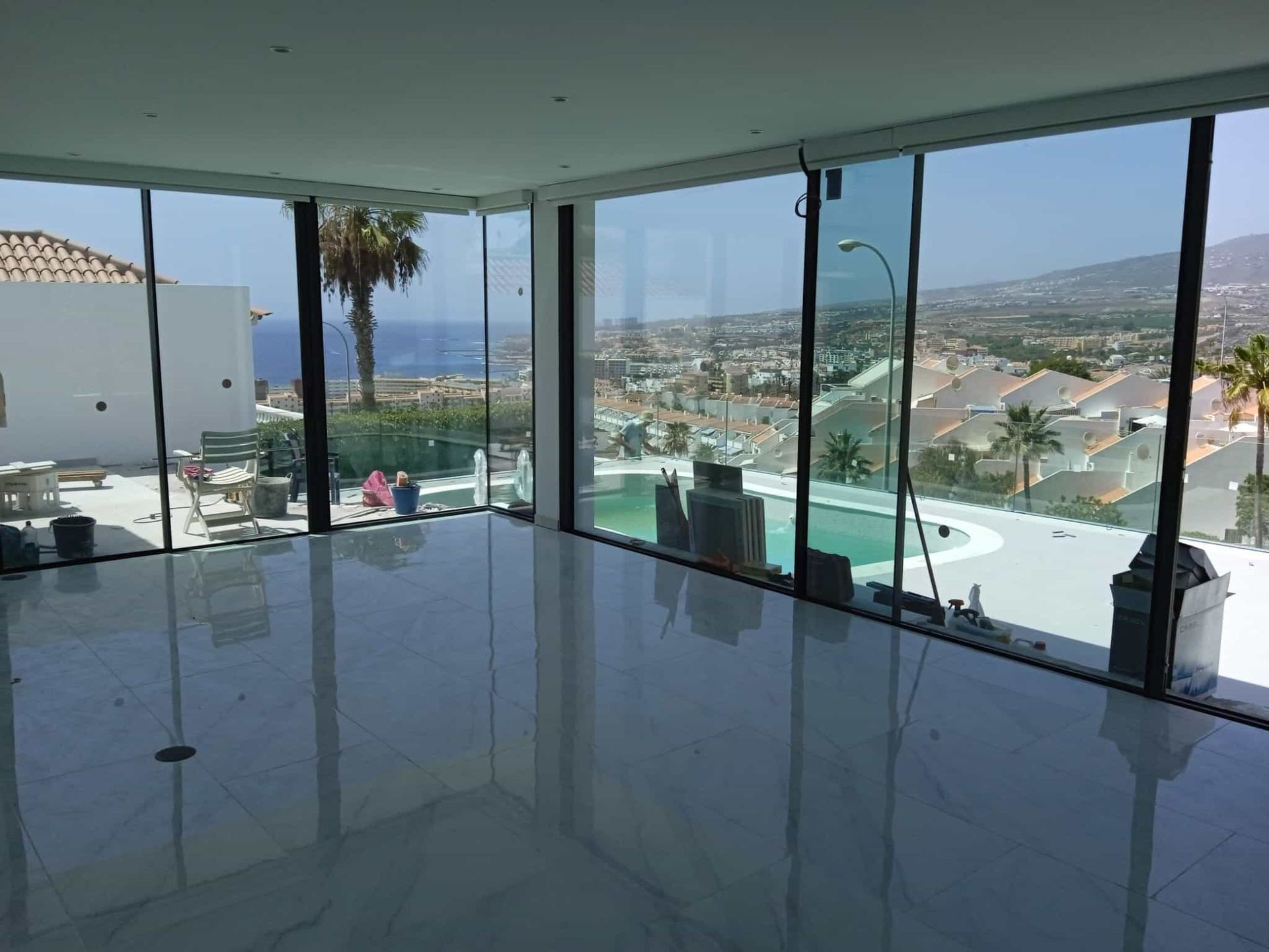 Una habitación moderna con grandes ventanales con vistas a la piscina y al paisaje urbano, bajo un cielo despejado.