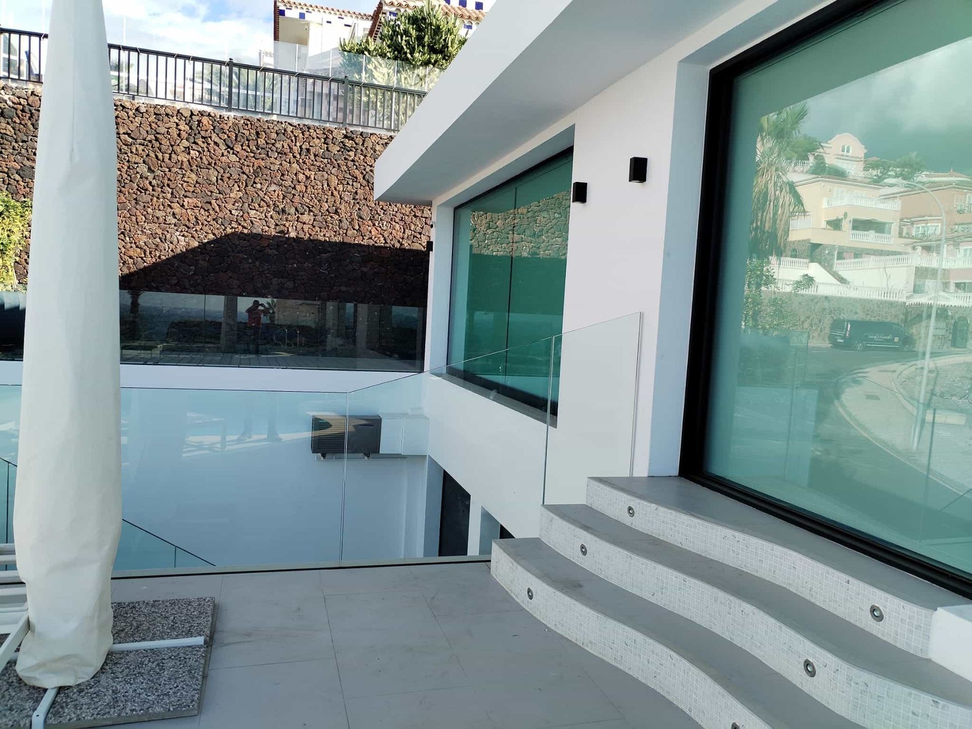 Edificio moderno con ventanas de vidrio, escalones y una barandilla transparente con vista al agua.