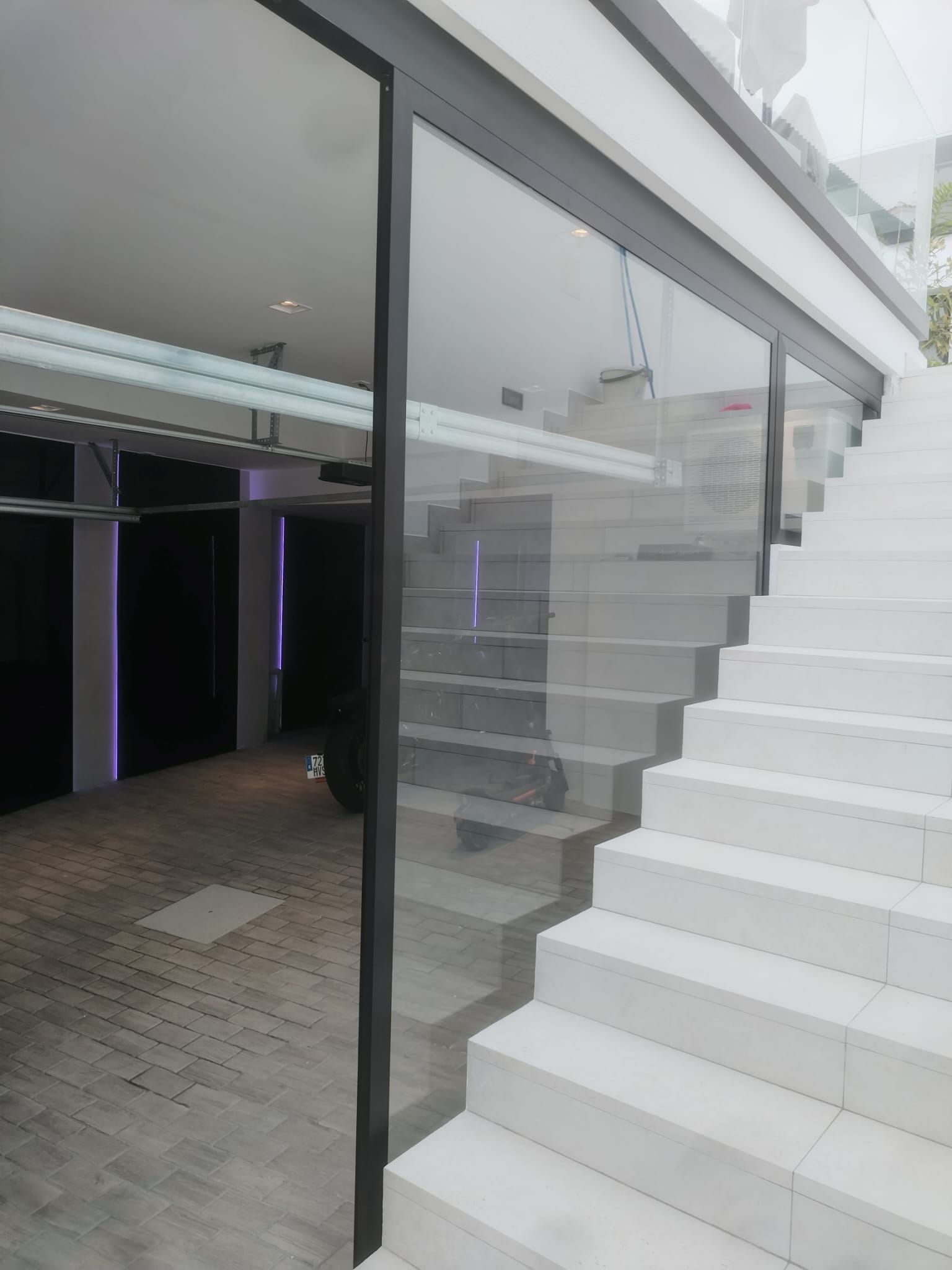 Edificio con paredes de cristal y escalera exterior blanca. Interior visible, con paredes negras y estética moderna.