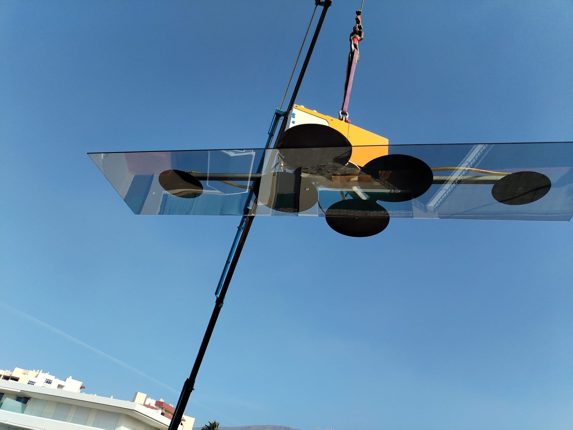Un gran panel de vidrio levantado por una grúa contra un cielo azul claro.