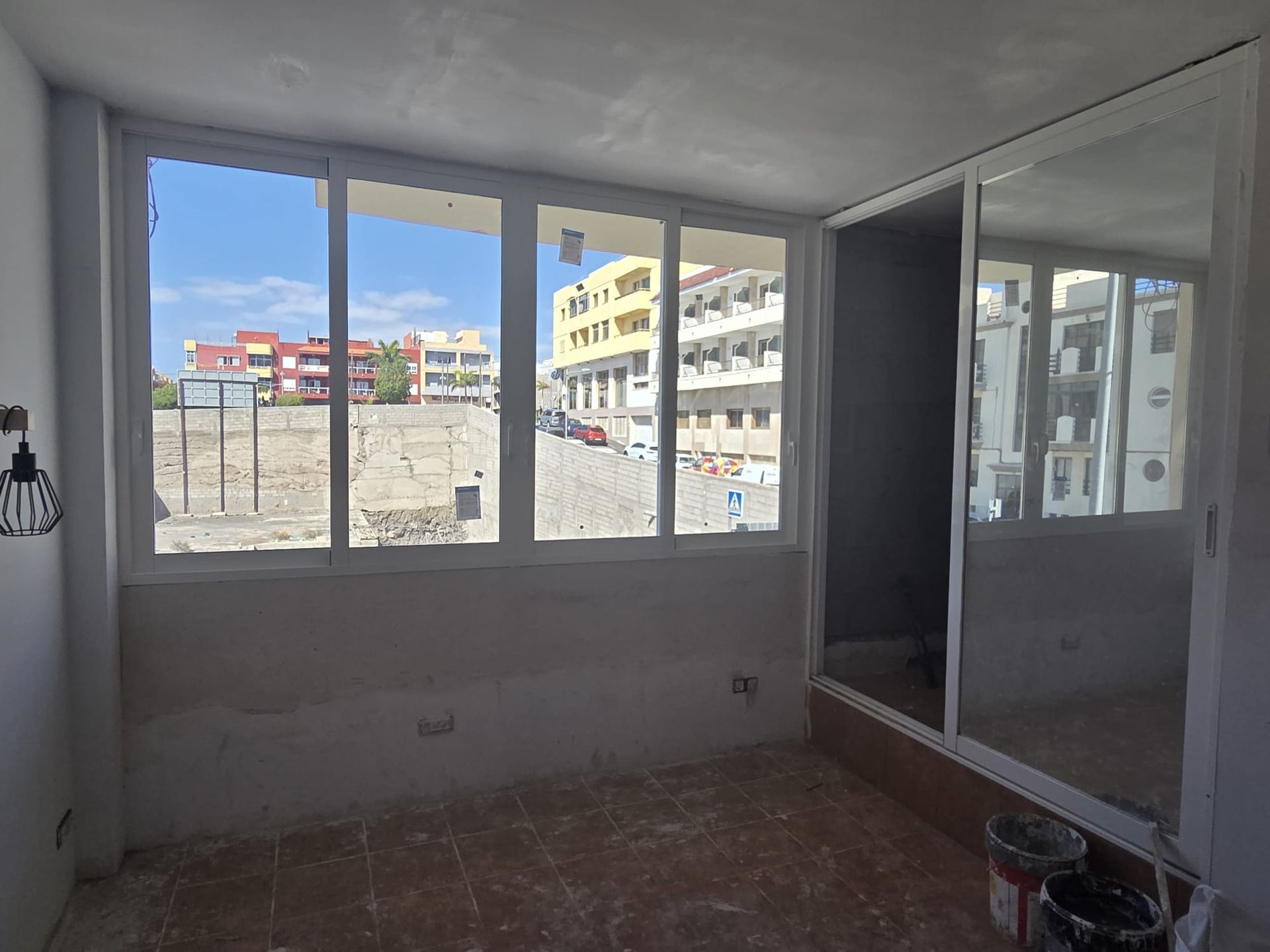 Habitación vacía con grandes ventanales, paredes sin terminar y un gran espejo corredizo.