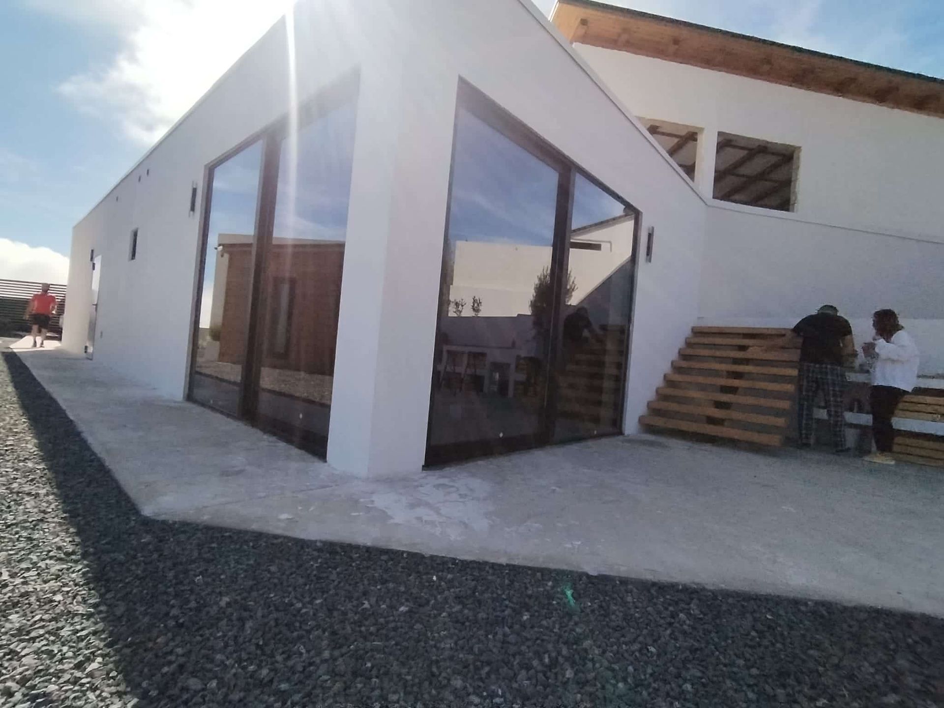 Edificio moderno blanco con grandes ventanales en el exterior. Dos personas cerca de palés de madera.