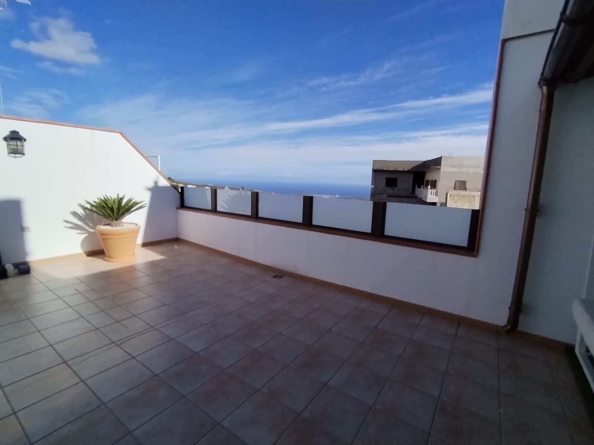 Terraza con piso de baldosas, paredes blancas y vista al océano azul bajo un cielo brillante.