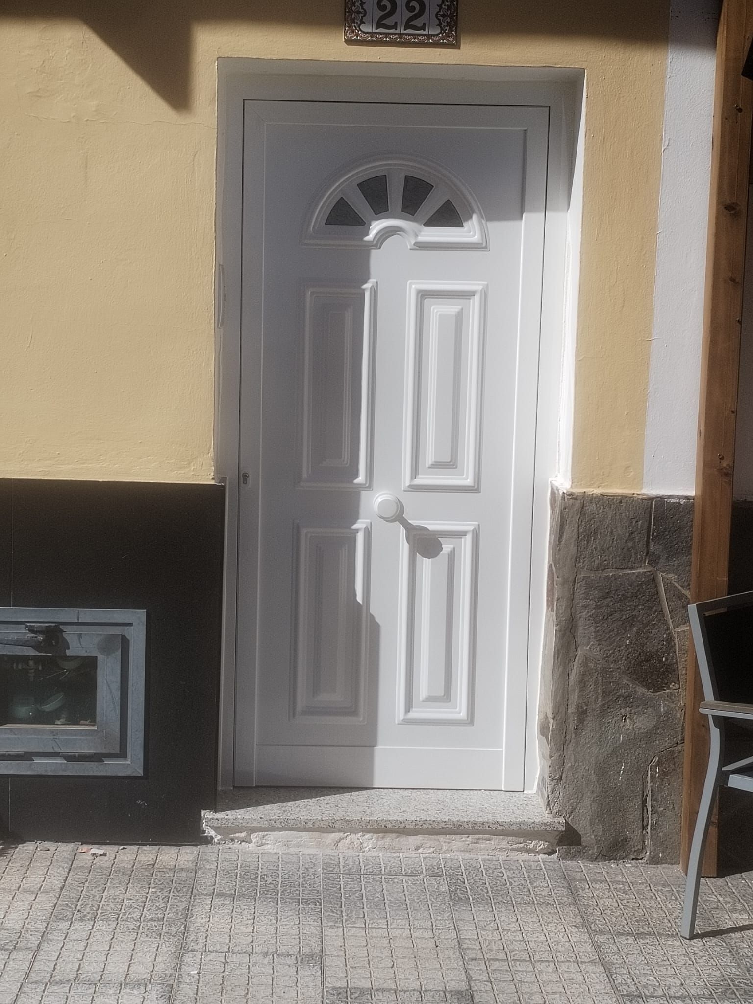 Puerta blanca con ventana arqueada en un edificio amarillo y blanco con un pequeño escalón y placa de dirección.
