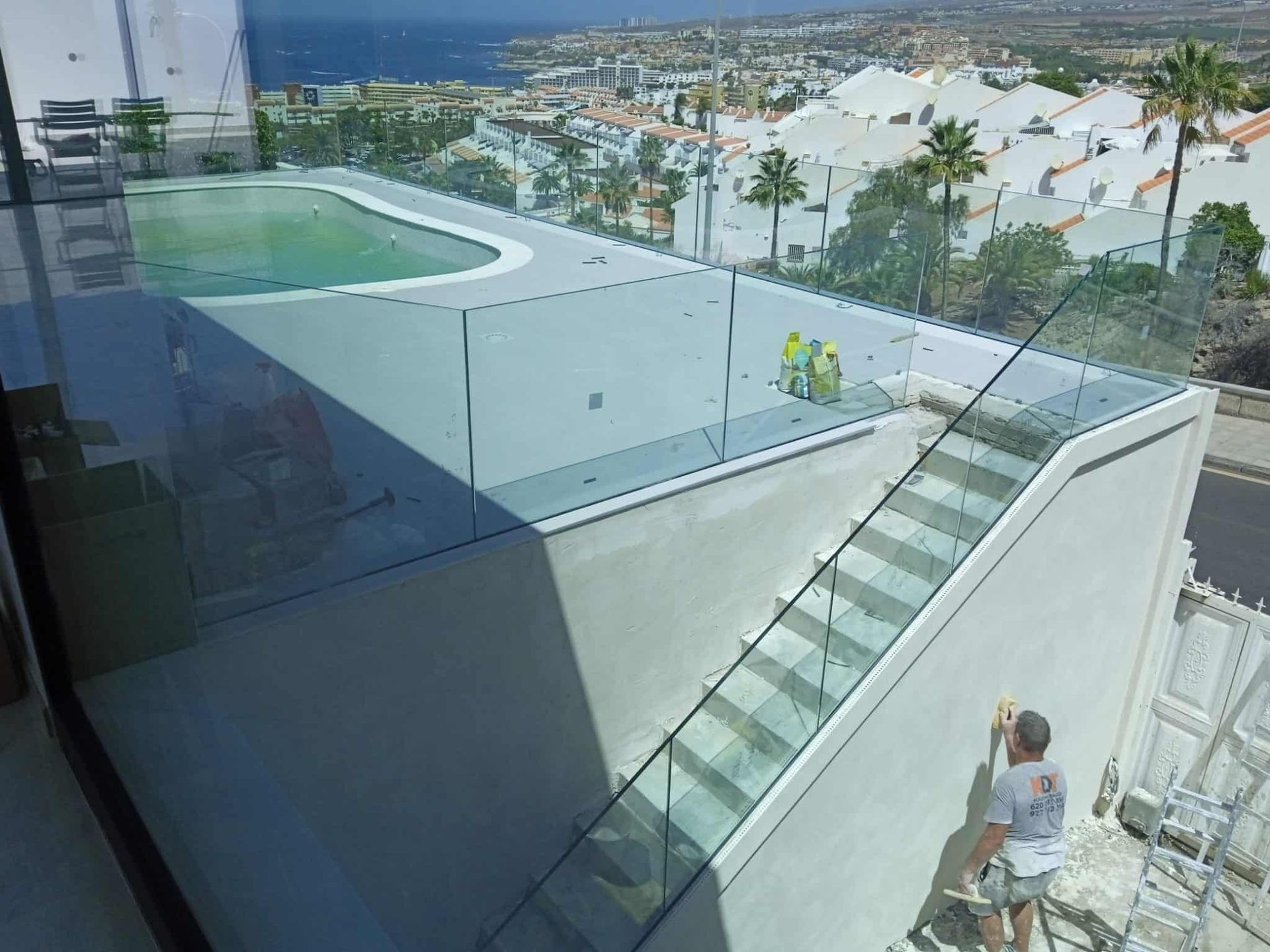 Vista exterior del edificio con piscina en la azotea, barandillas de cristal y escaleras. Se ven dos trabajadores y un hombre.