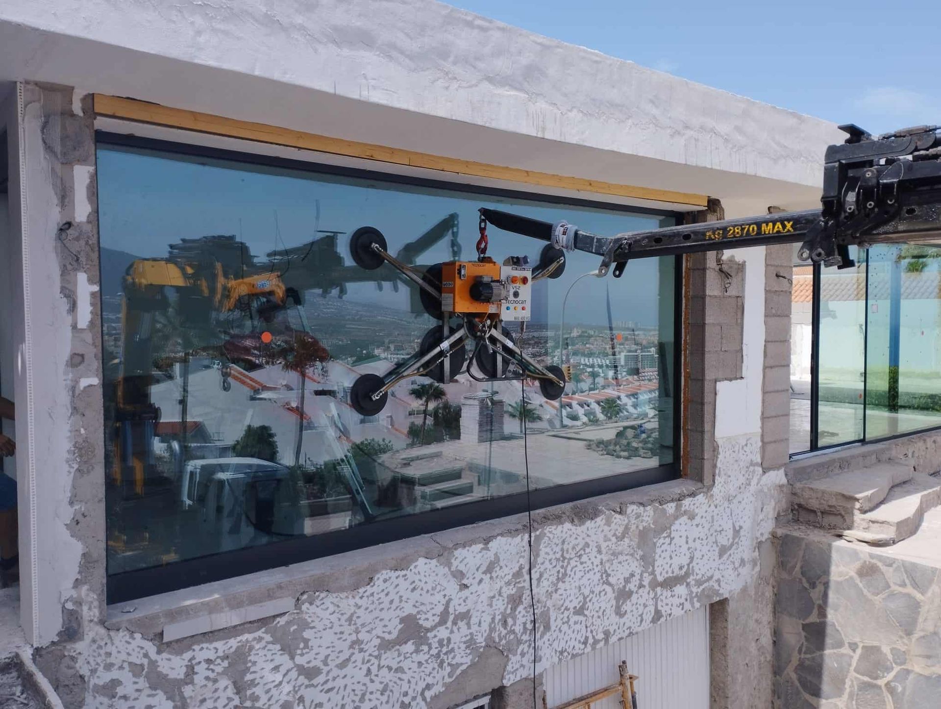 Un brazo robótico con ventosas está instalando una gran ventana de vidrio en la fachada de un edificio.