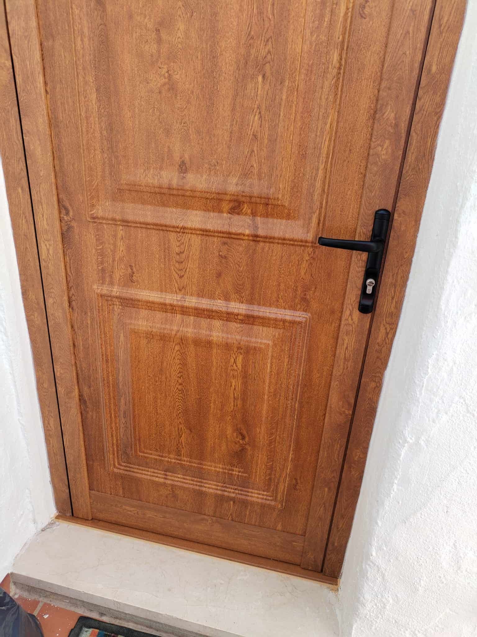 Puerta de madera marrón con tirador y moldura de color negro.