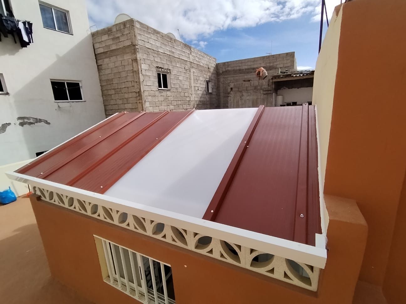 Techo con metal marrón y paneles translúcidos blancos en un edificio naranja; cielo azul en el fondo.
