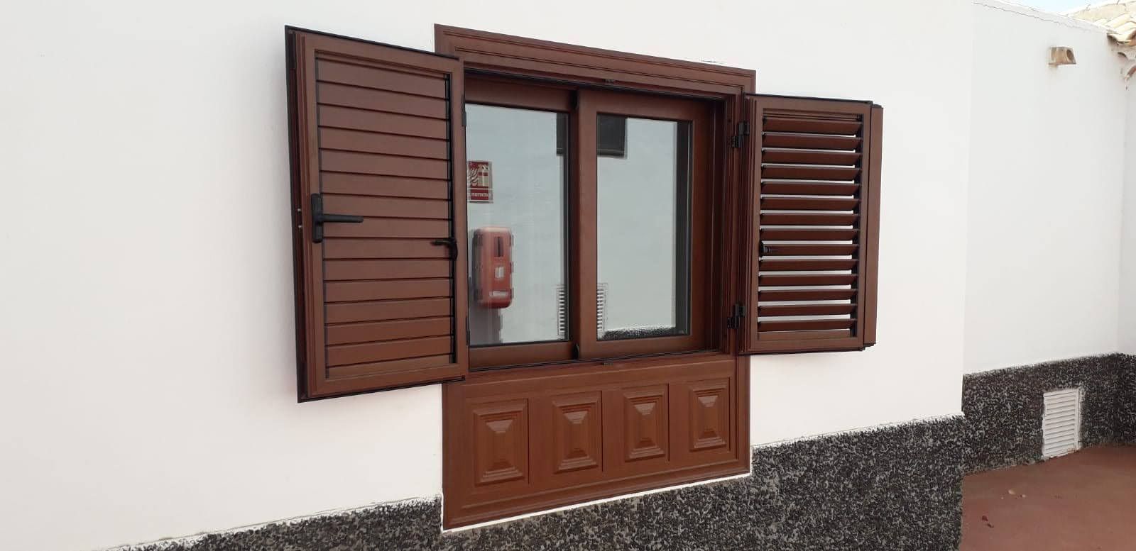 Ventana marrón con contraventanas sobre una pared blanca. Las contraventanas están abiertas.