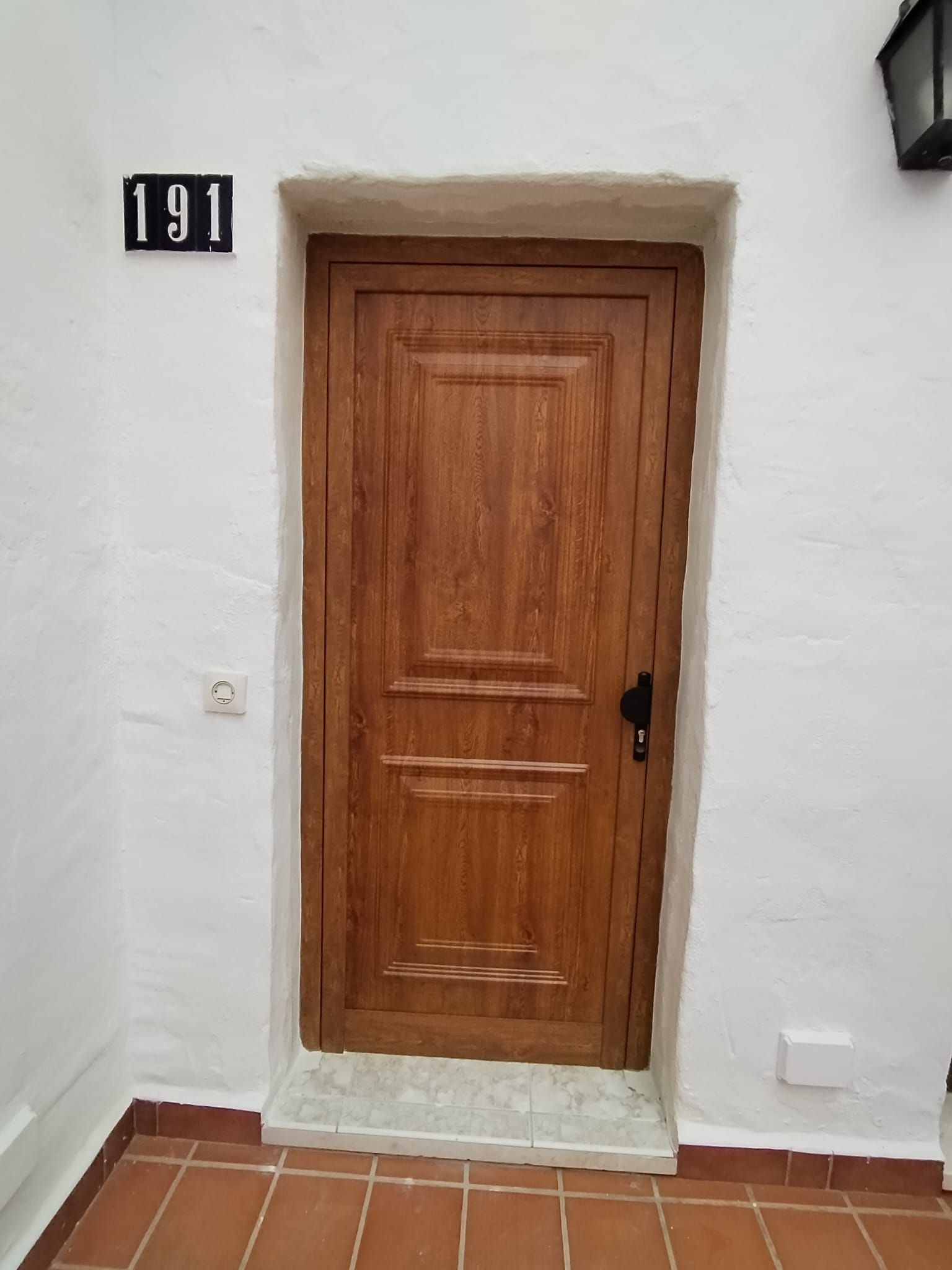 Puerta de madera con tirador negro y número 191 sobre pared blanca.
