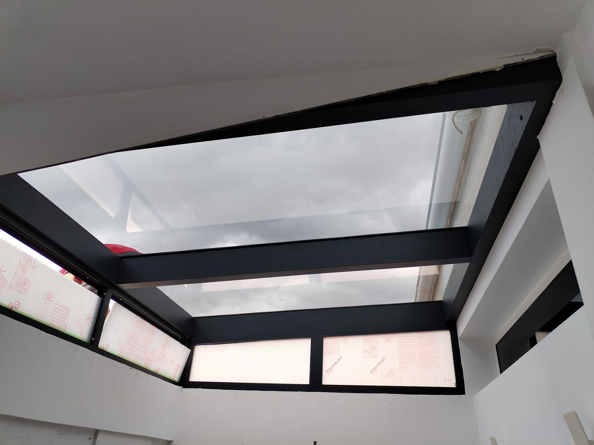 Tragaluz en una habitación de paredes blancas con marco gris oscuro y vidrio transparente.