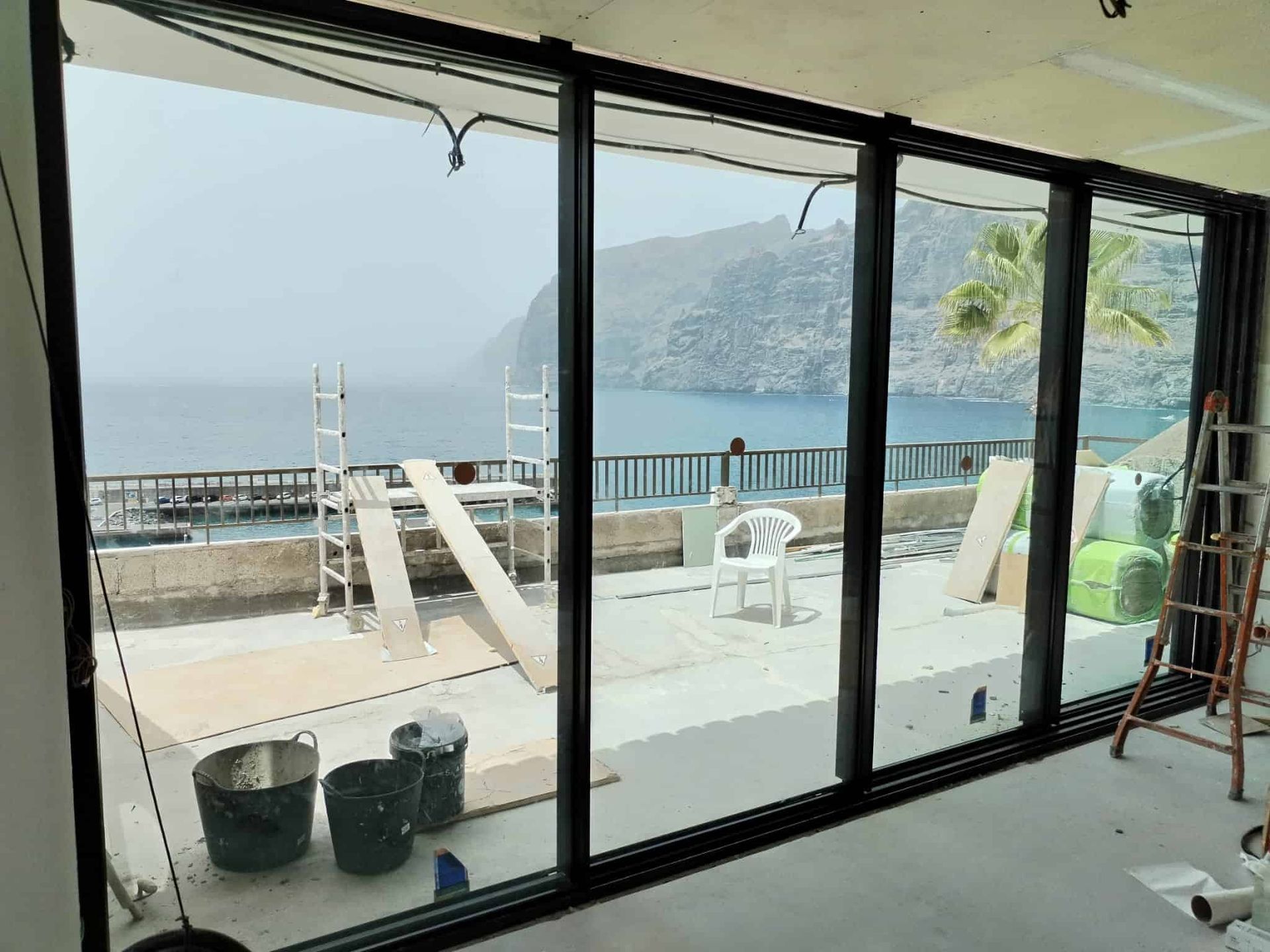 Grandes puertas de cristal ofrecen vistas a la costa. Herramientas y materiales de construcción en la terraza.