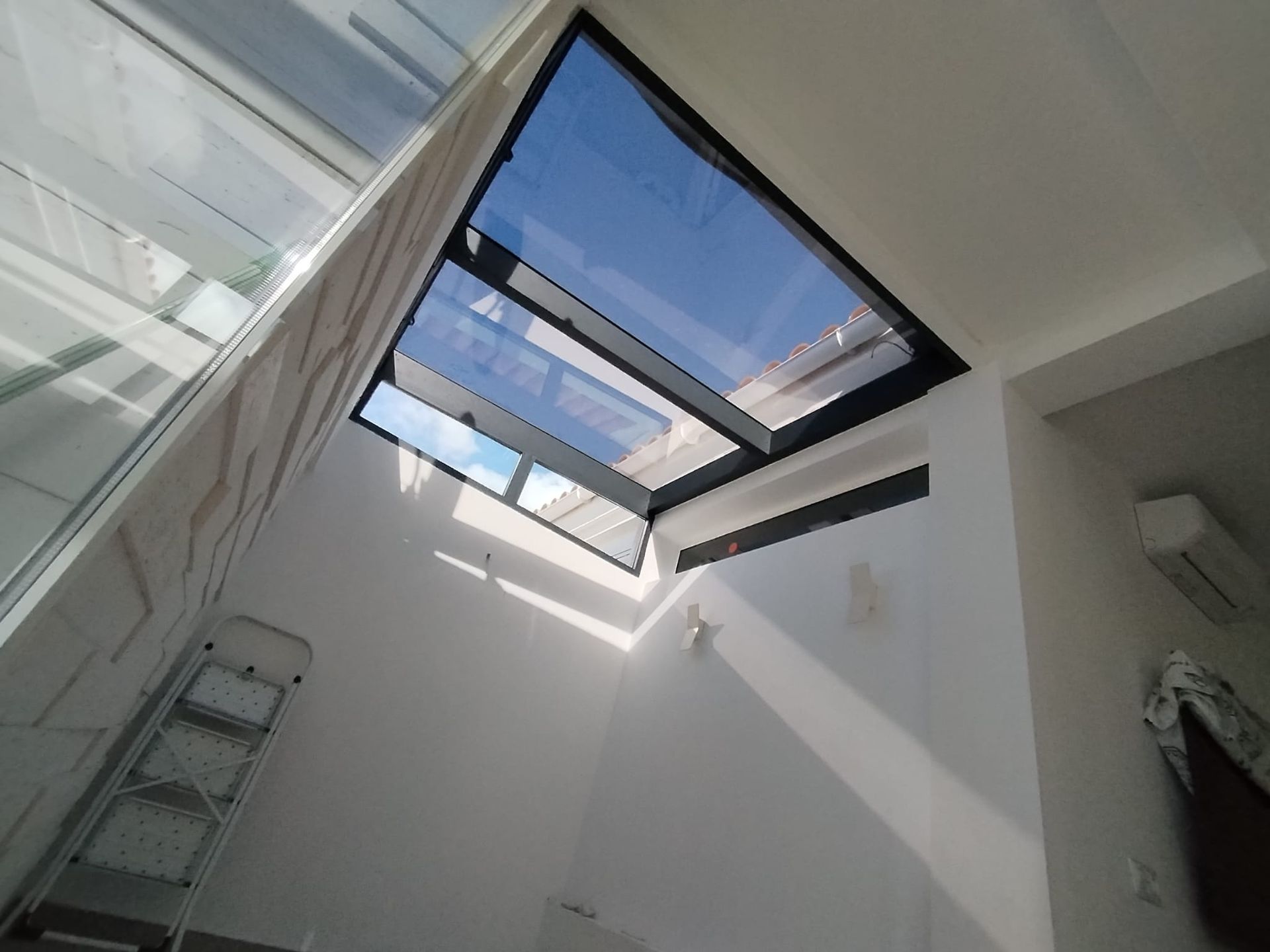 Mirando hacia arriba a una habitación de paredes blancas con una claraboya grande y abierta. Hay una escalera en la esquina.