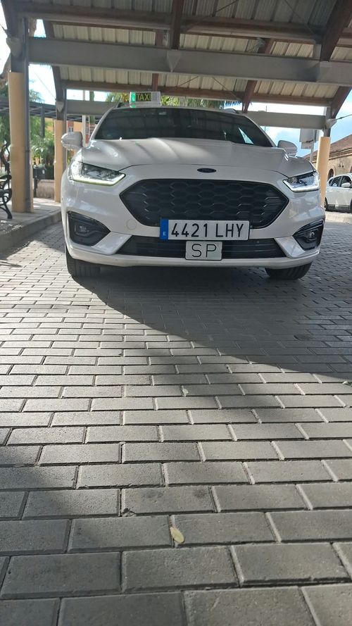 Un taxi blanco con pegatinas en la ventana, estacionado en una calle de la ciudad.