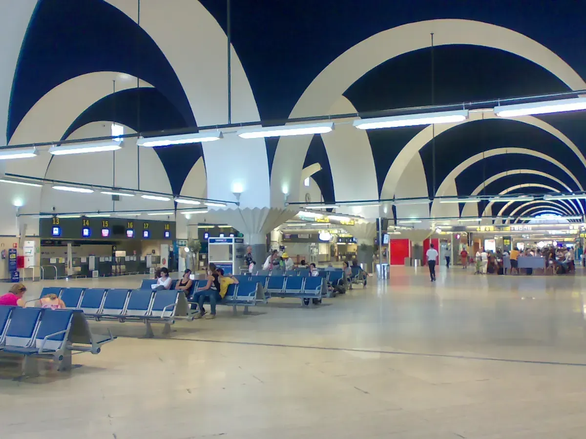 Interior del aeropuerto con techo abovedado, asientos y mostradores de facturación.