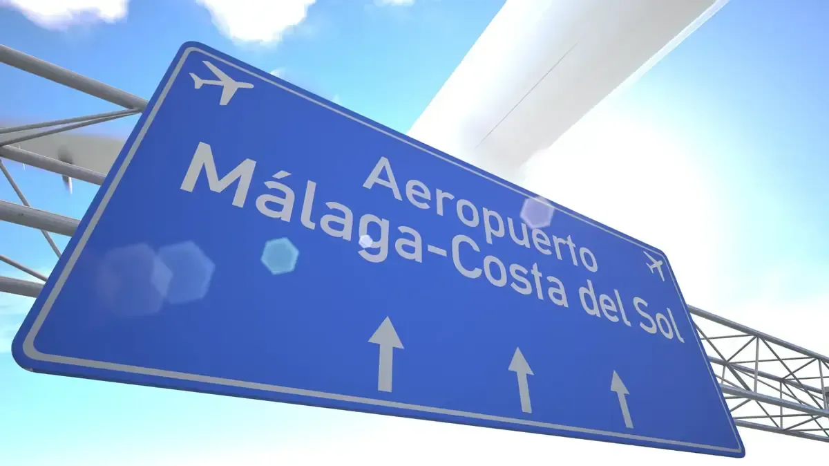 Señal azul del Aeropuerto de Málaga-Costa del Sol, con iconos de aviones y flechas, sobre un cielo azul.