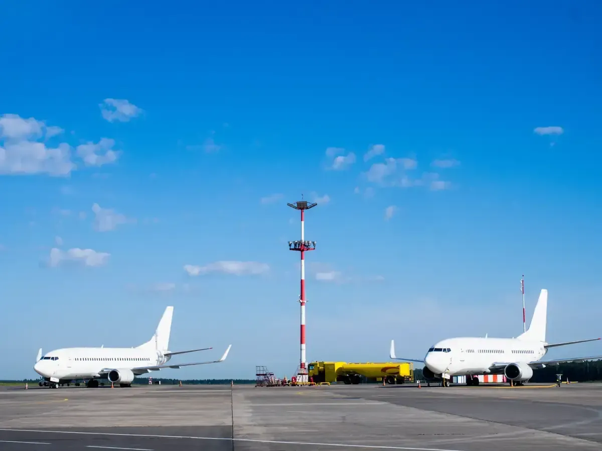 Dos aviones blancos estacionados en un aeropuerto en un día soleado con una alta torre de comunicaciones.
