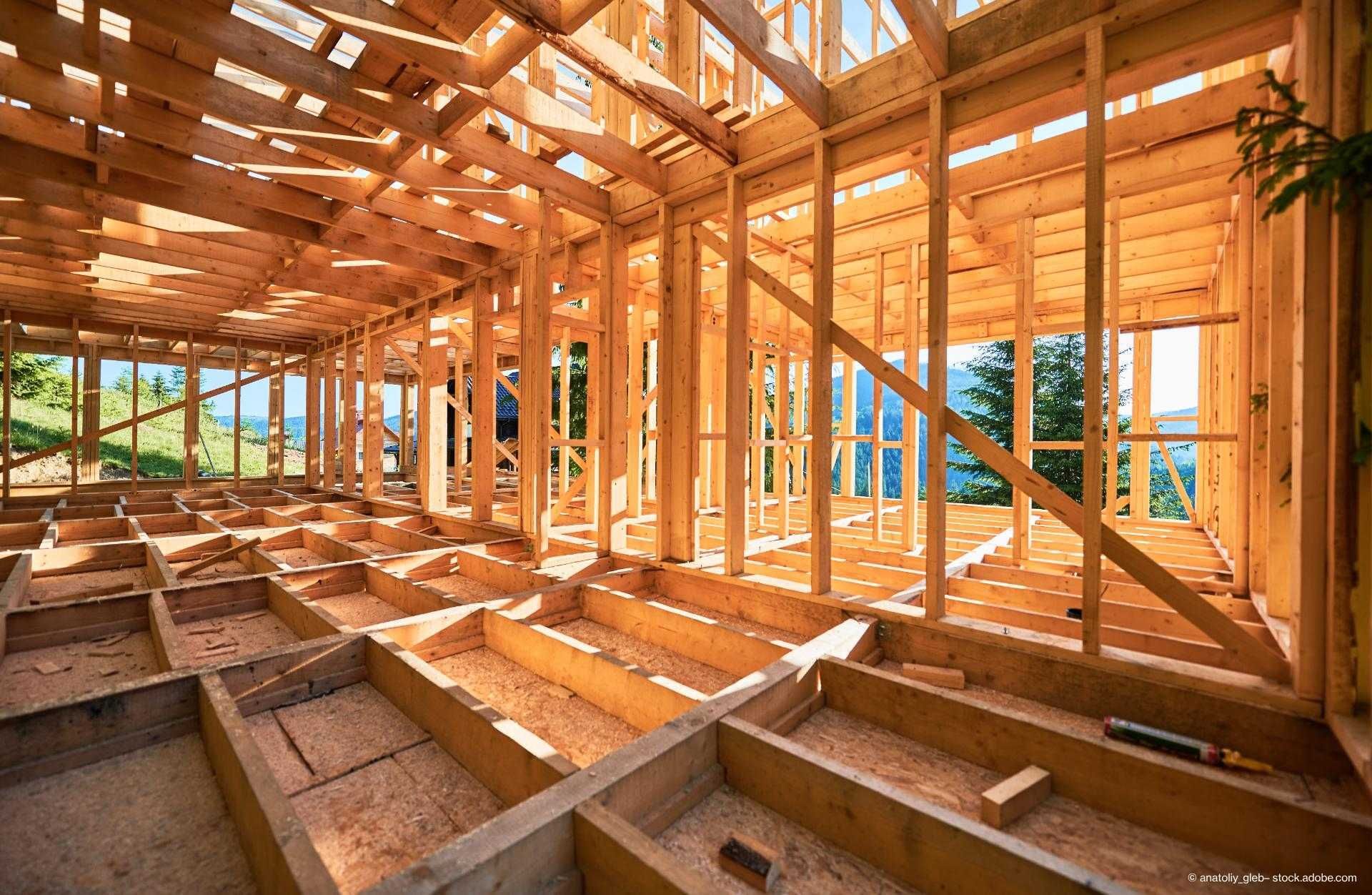 Holzrahmenbau eines Hauses im Rohbau, mit freiliegender Struktur und Blick auf Bäume und Berge im Hintergrund.