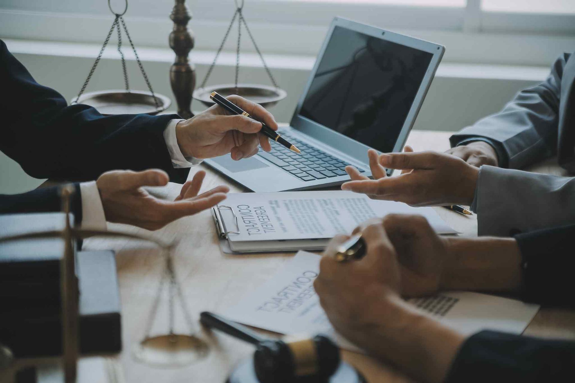 Un grupo de profesionales con traje discuten documentos y un ordenador portátil en una mesa con reglas legales y un mazo.