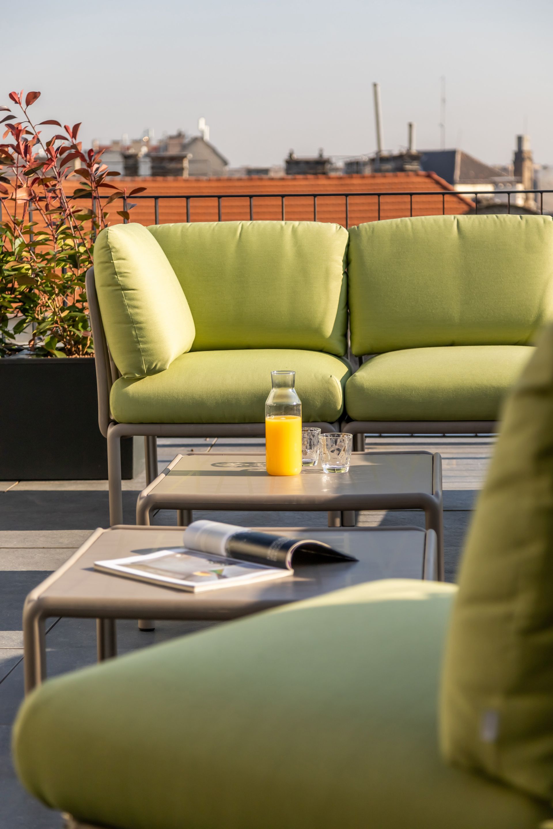 Outdoor lounge area with lime green sofa, orange juice, and a magazine on a rooftop in Marone Suites Budapest.