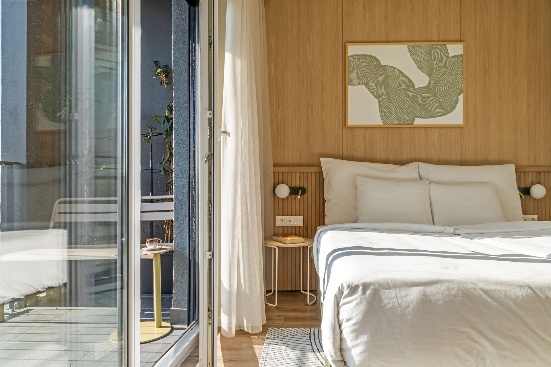 Bright bedroom with a white bed, wooden walls, and a balcony visible through a glass door in Marone Suites Budapest.