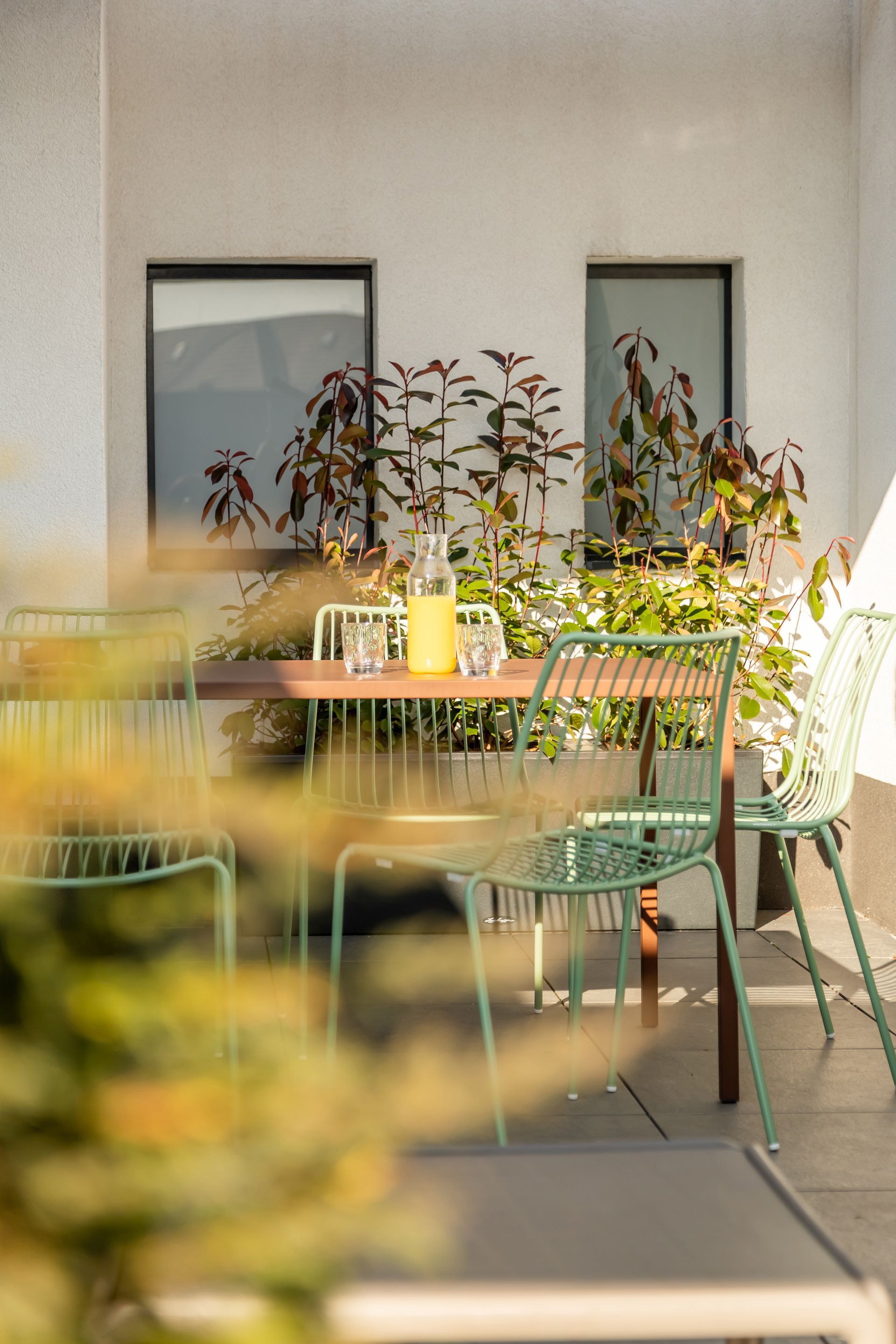 Outdoor patio with table for 6, green chairs, and plants. A pitcher and glasses sit on the table in Marone Suites Budapest.