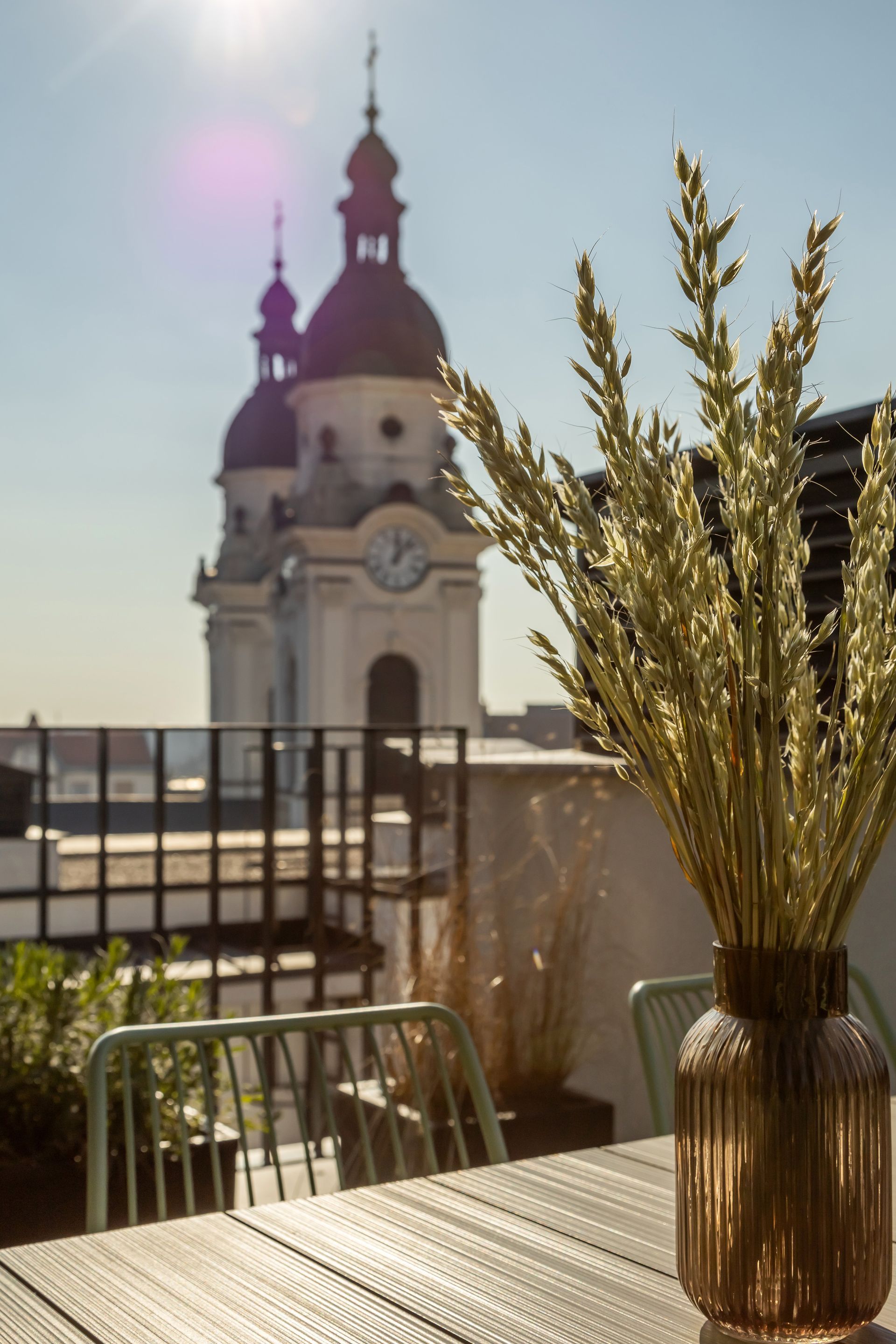 Golden wheat in a vase on a rooftop, with a church steeple in the blurred background in Marone Suites Budapest.