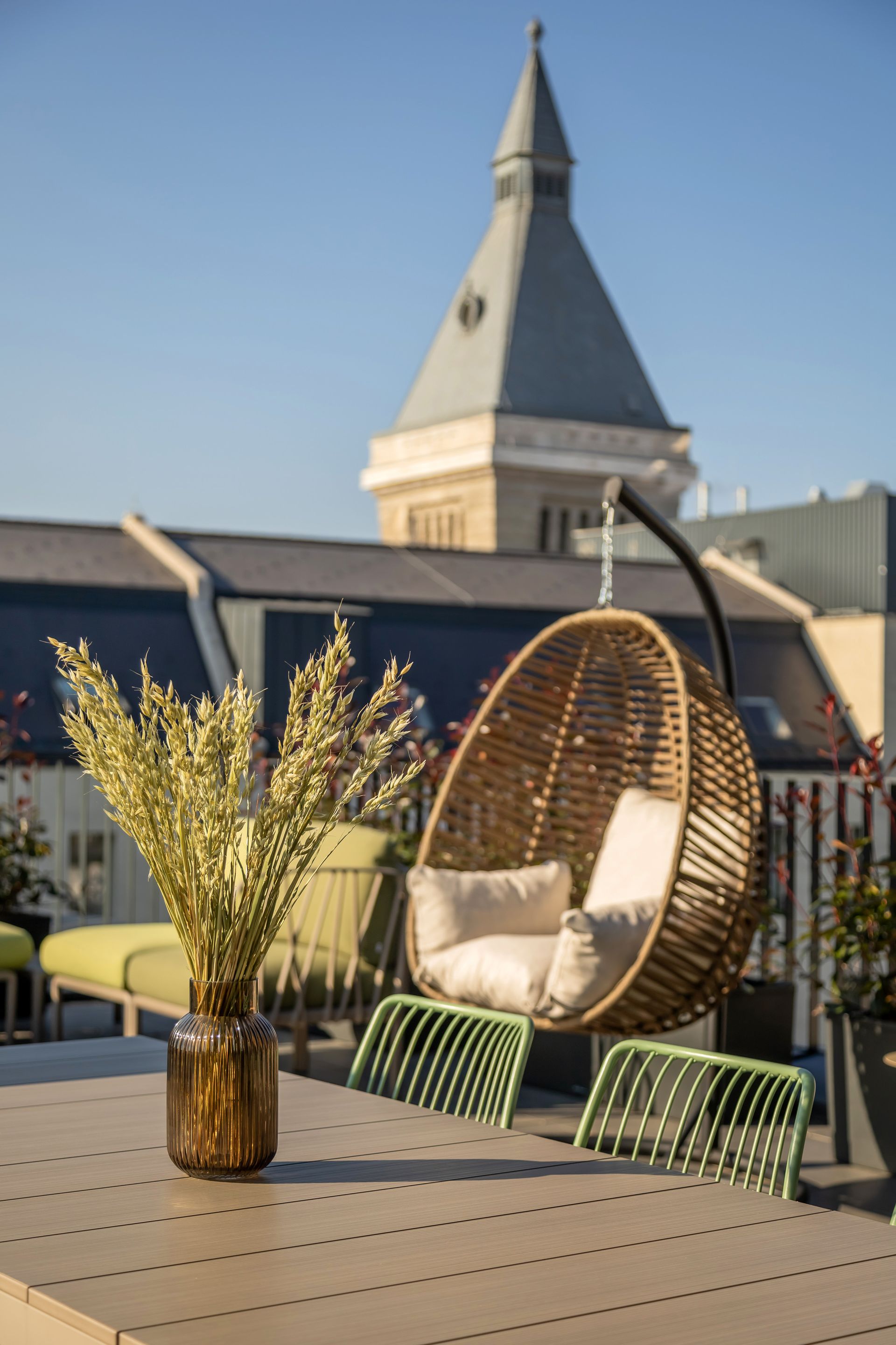 Rooftop patio with hanging chair, table, vase of flowers, and cityscape in Marone Suites Budapest.