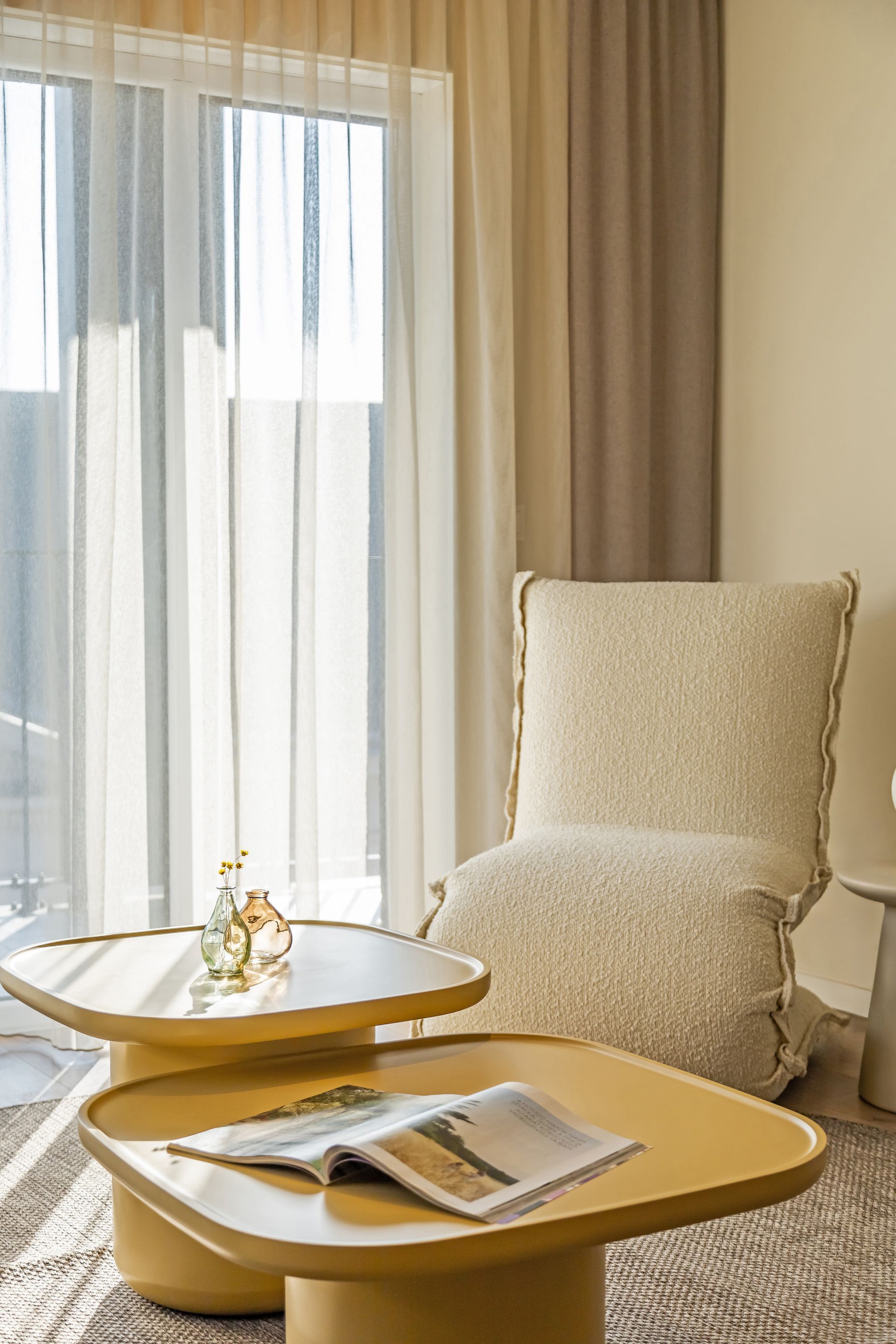 Living room with a yellow layered coffee table, cream textured armchair, and sheer curtains in Marone Suites Budapest.