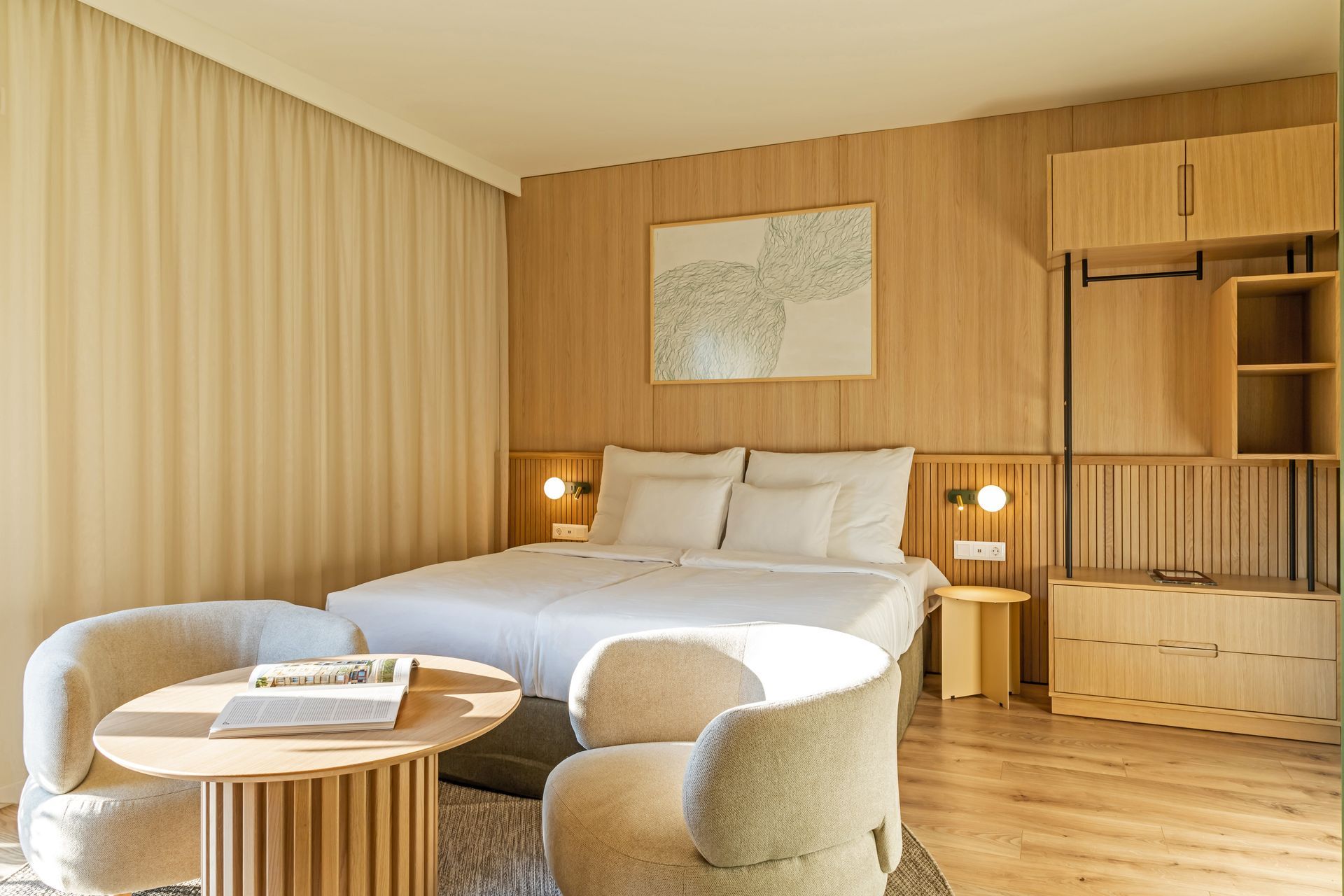 Studio apartment with a double bed, two armchairs, a table, and light wooden paneling in Marone Suites Budapest.