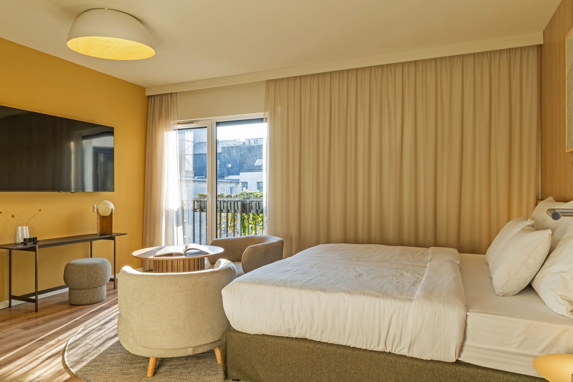 Studio apartment with bed, lounge chairs, and a window with natural light and a view in Marone Suites Budapest.