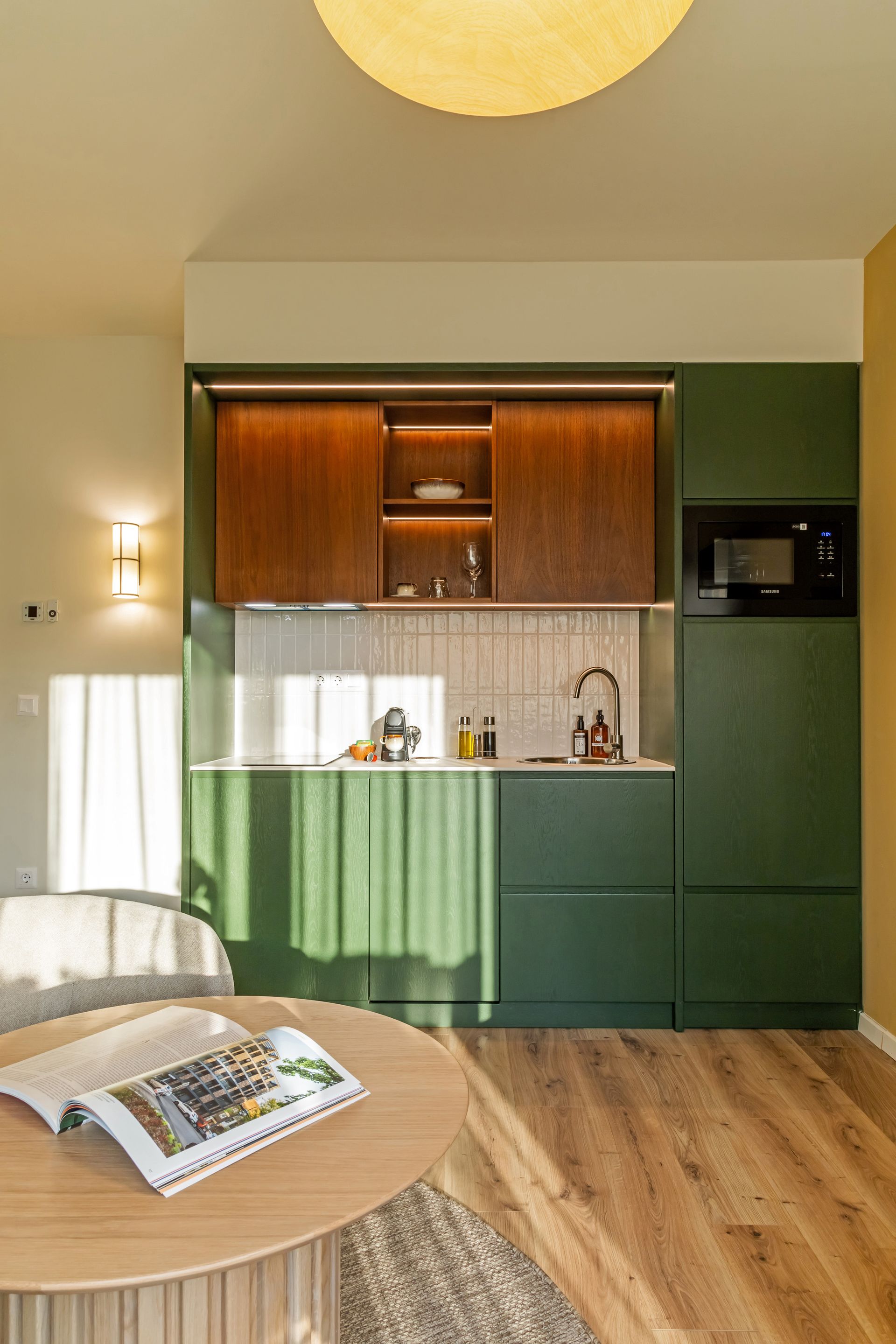 Modern kitchen with dark green cabinets, wooden accents, and a round table with a magazine in Marone Suites Budapest.