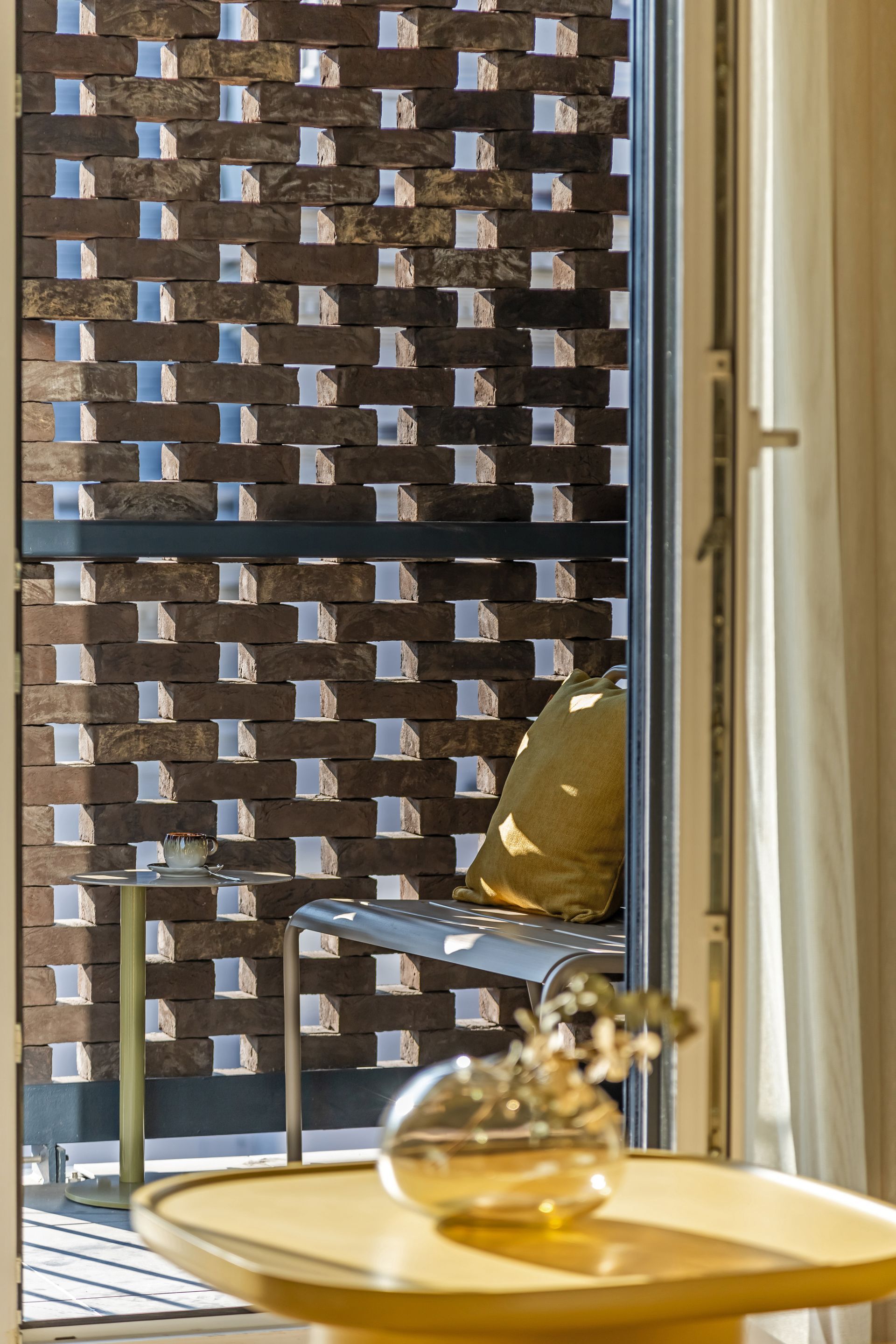 Balcony view: open door reveals a chair with a pillow and decorative brick wall with window squares in Marone Suites.