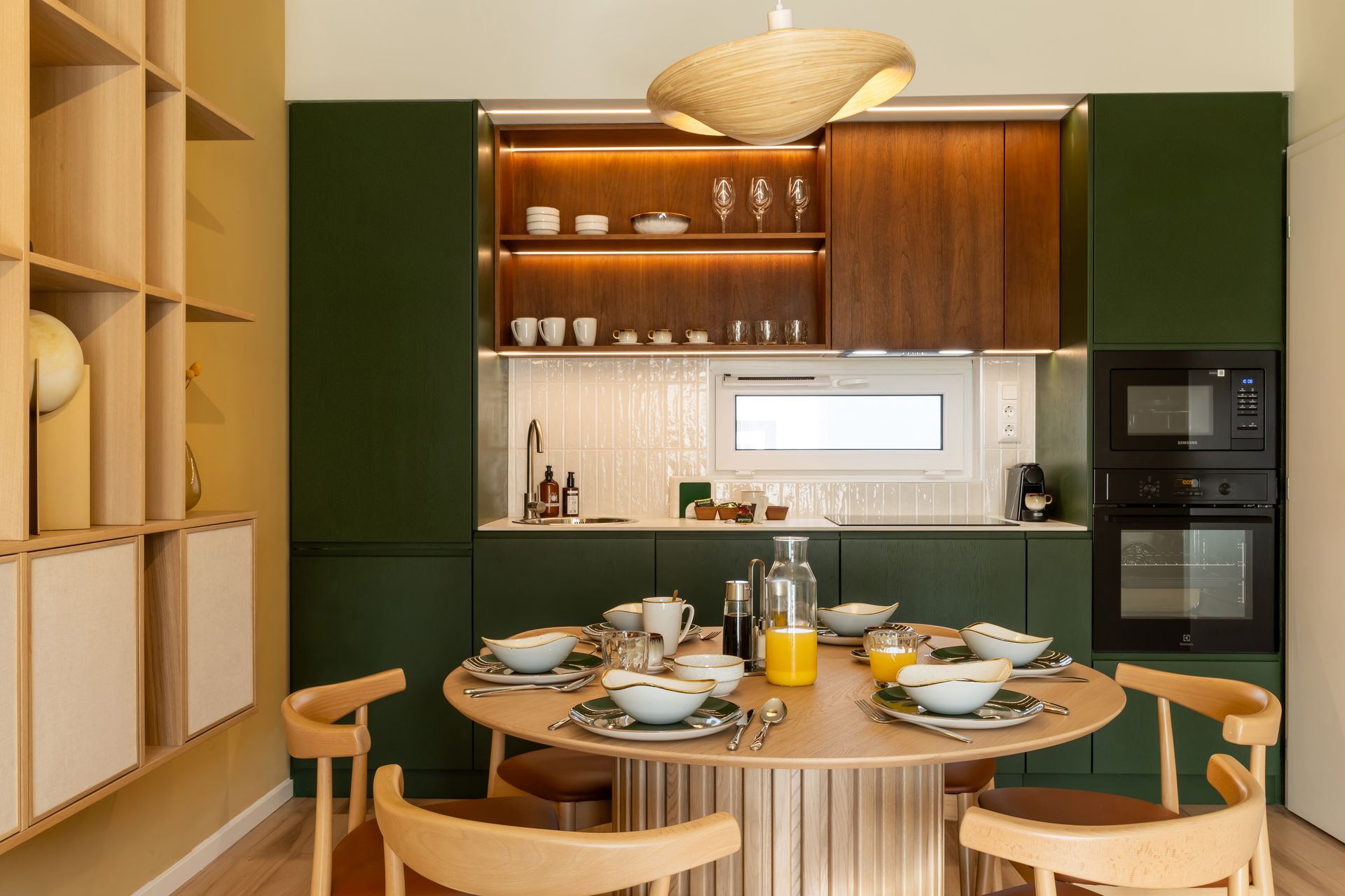 Green and wood fully equipped kitchen with round table set for a meal in Marone Suites Budapest.