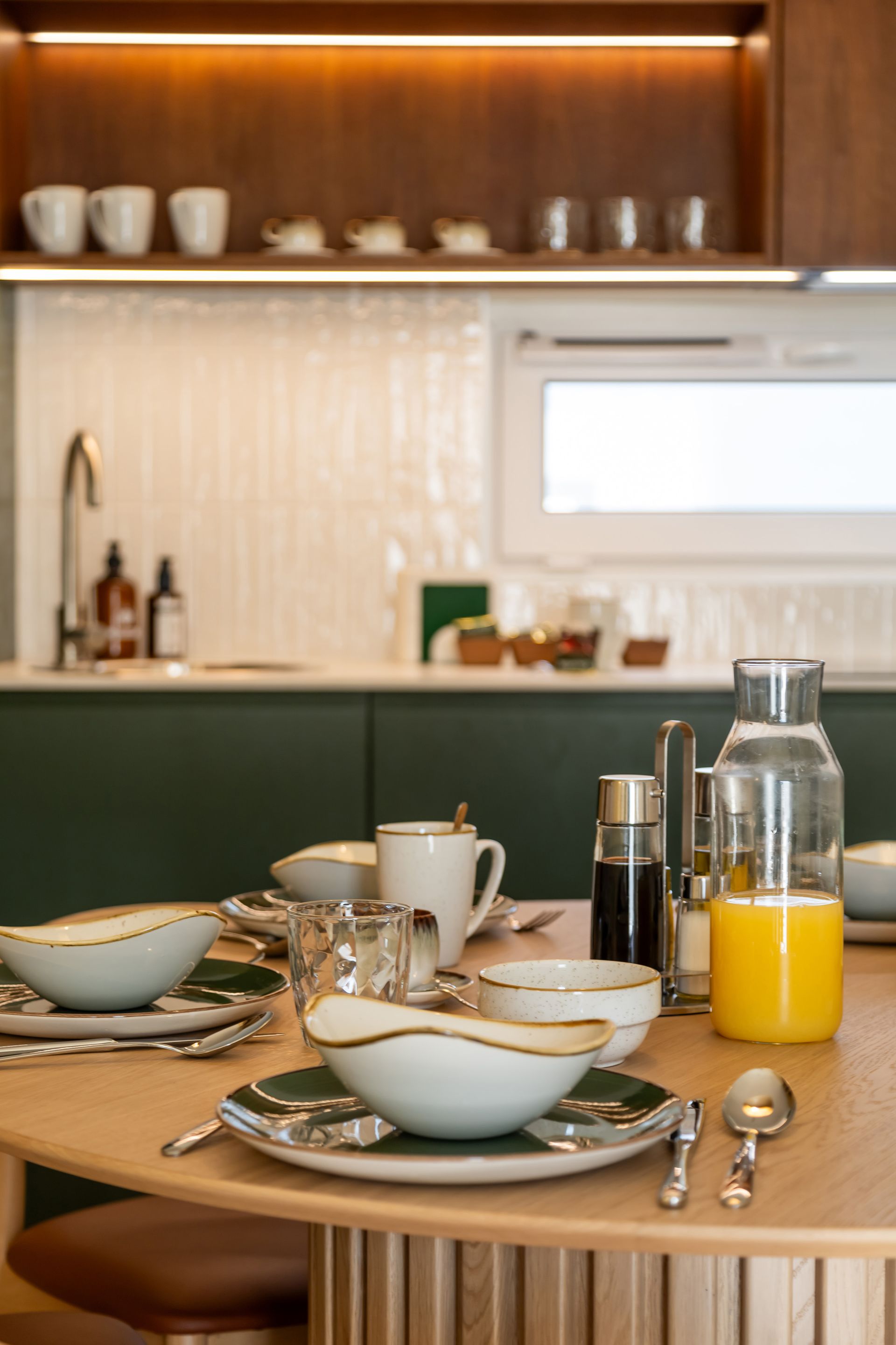 Breakfast table set with plates, bowls, silverware, and a carafe of orange juice in a modern kitchen Marone Suites Budapest.
