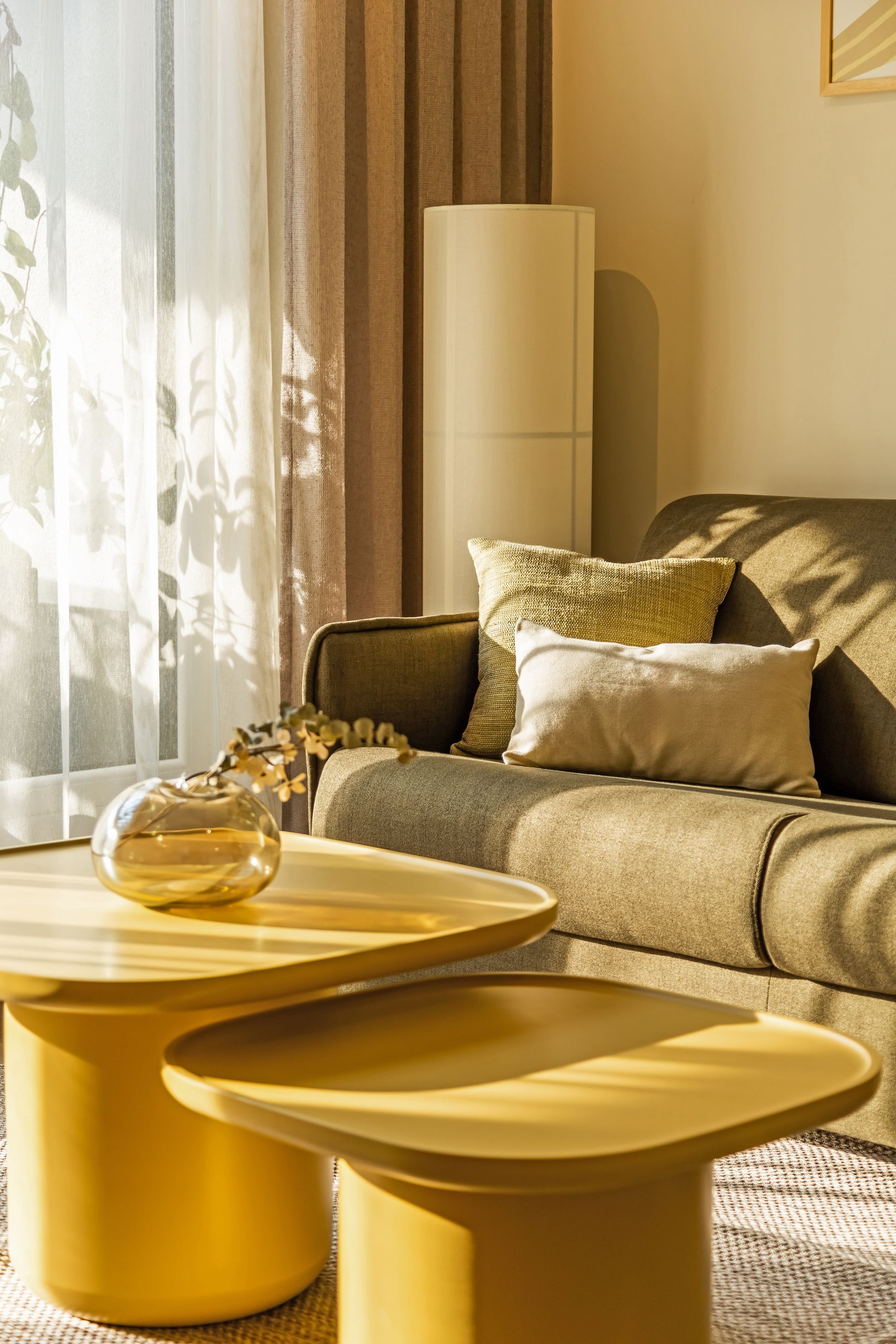 Living room with olive-green sofa, yellow coffee tables, sheer curtain and lots of light in Marone Suites Budapest.
