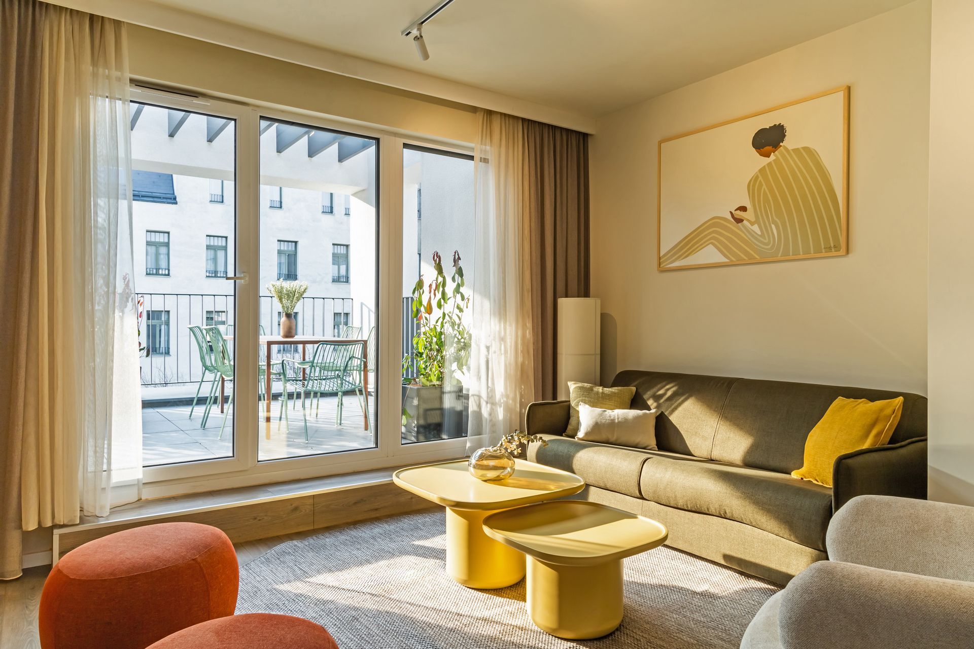Living room with sofa, coffee table, and balcony access. Bright with beige and orange accents in Marone Suites Budapest.