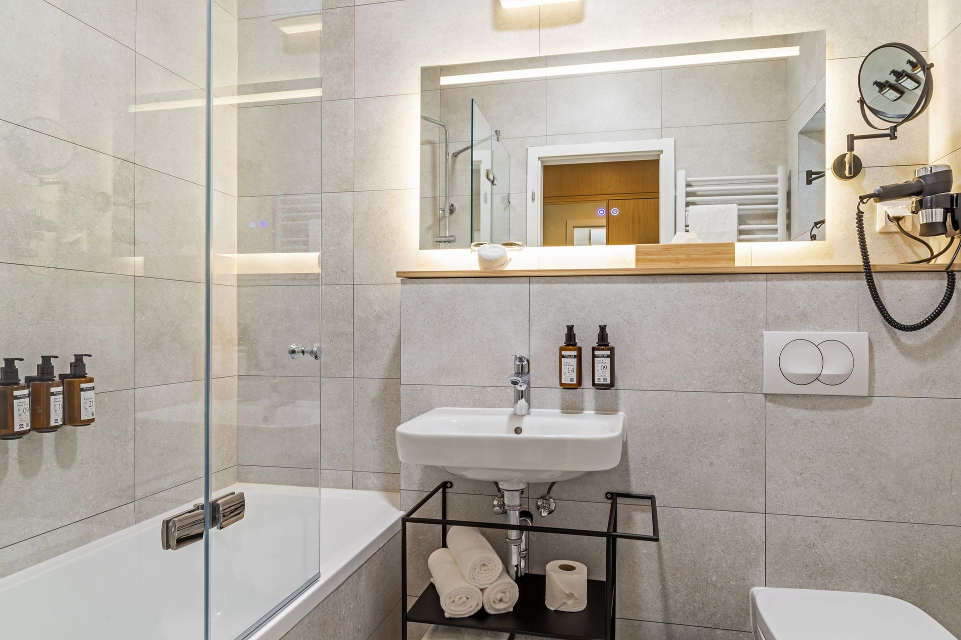 Modern bathroom with a bathtub, sink, mirror, toiletries and towels. Gray and white color scheme in Marone Suites Budapest.
