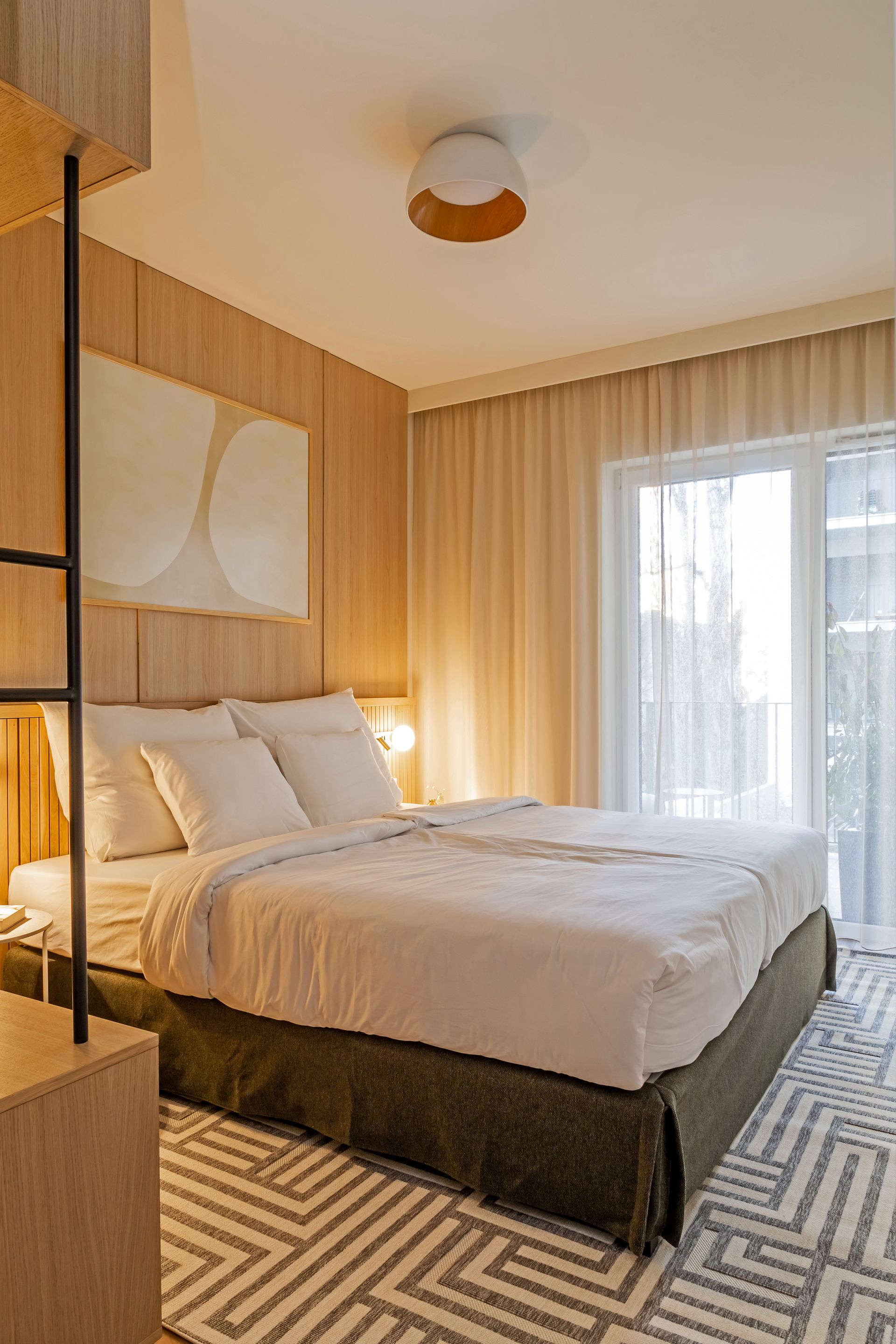 Cozy bedroom with a double bed, light wood paneling, artwork, and patterned rug in Marone Suites Budapest.