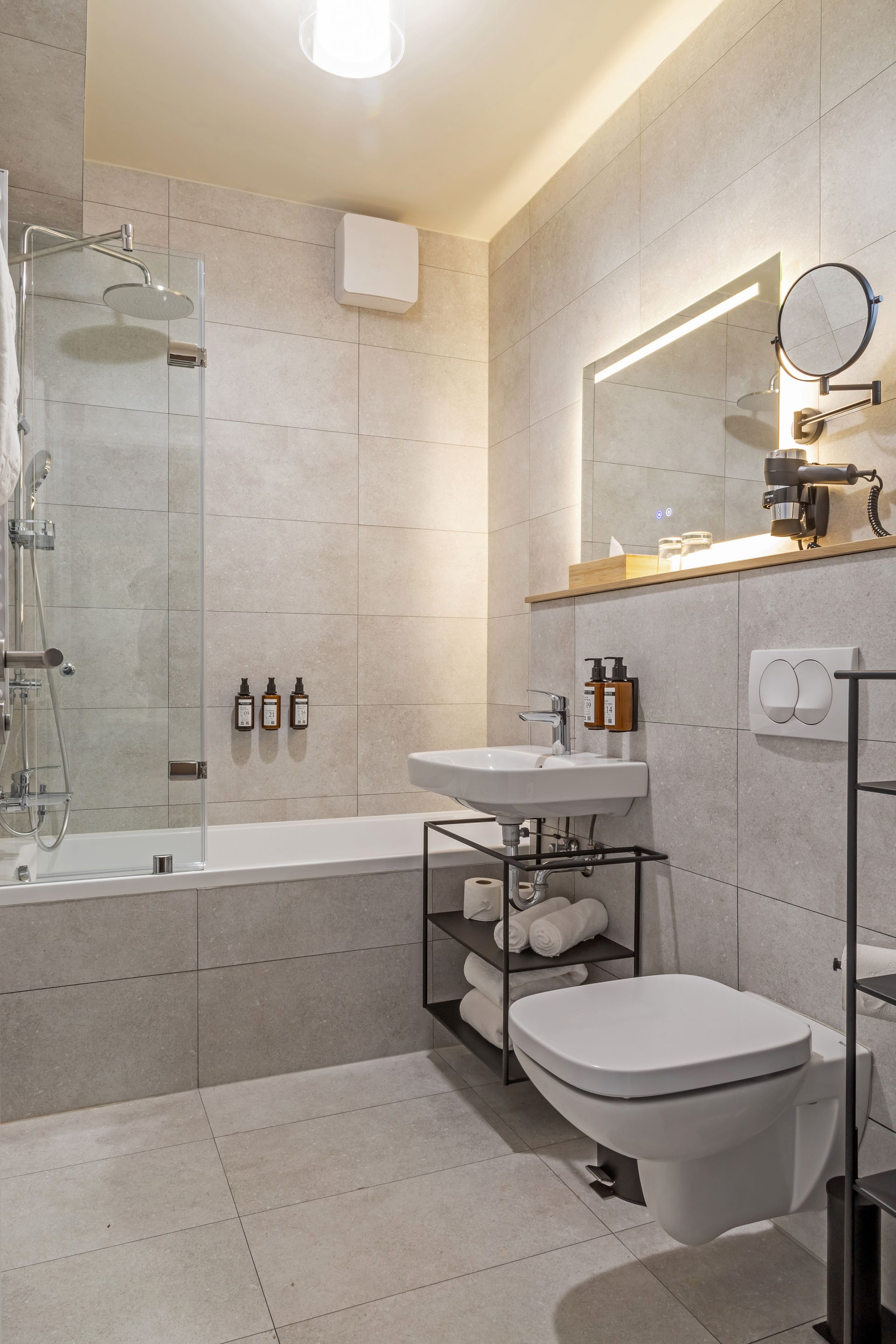Modern bathroom with a bathtub, shower, shampoo, conditioner, body cream and towels in Marone Suites Budapest.