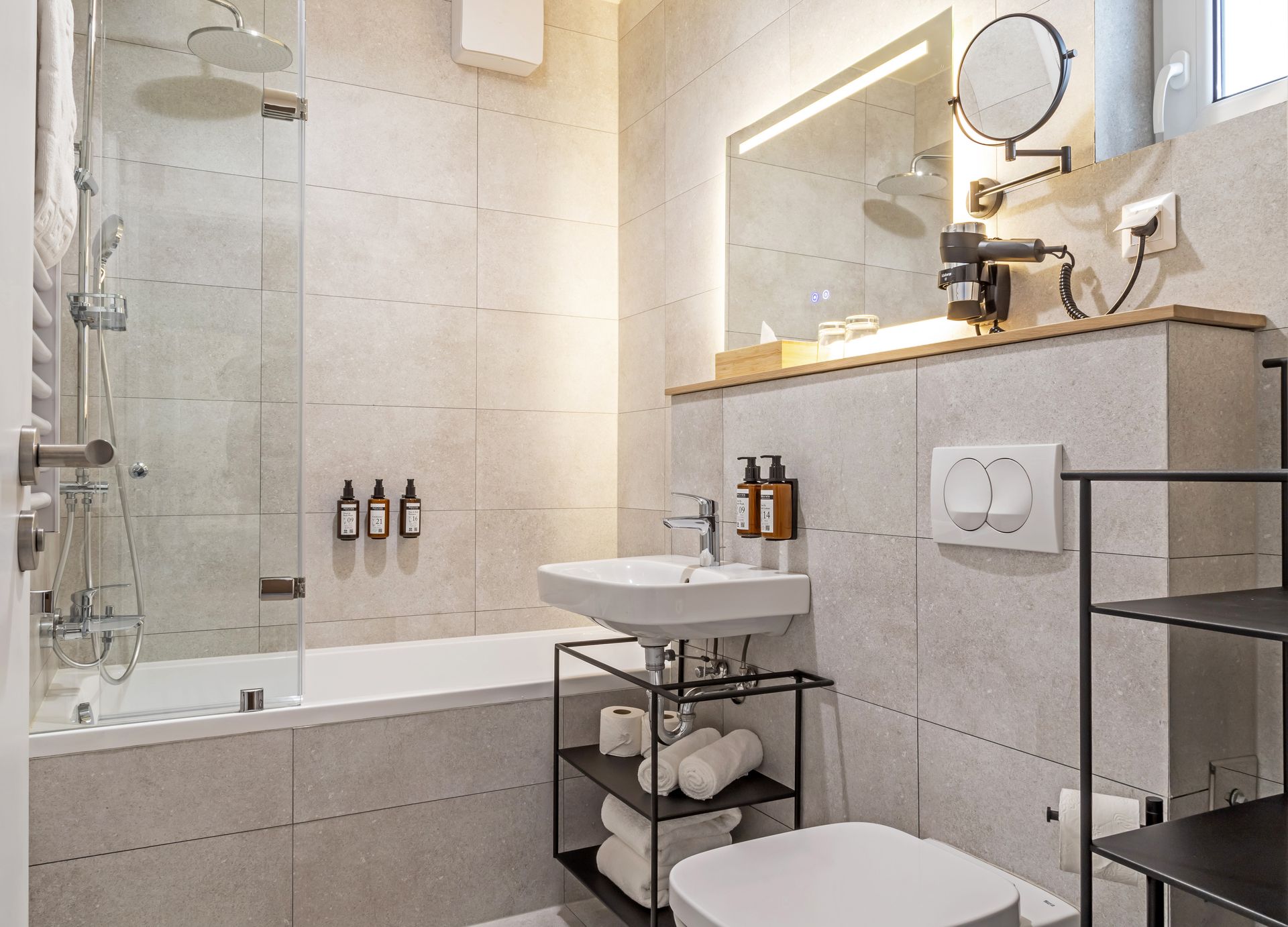 Modern bathroom with a shower, bathtub, sink, shampoo, conditioner, body cream, and towels in Marone Suites Budapest.