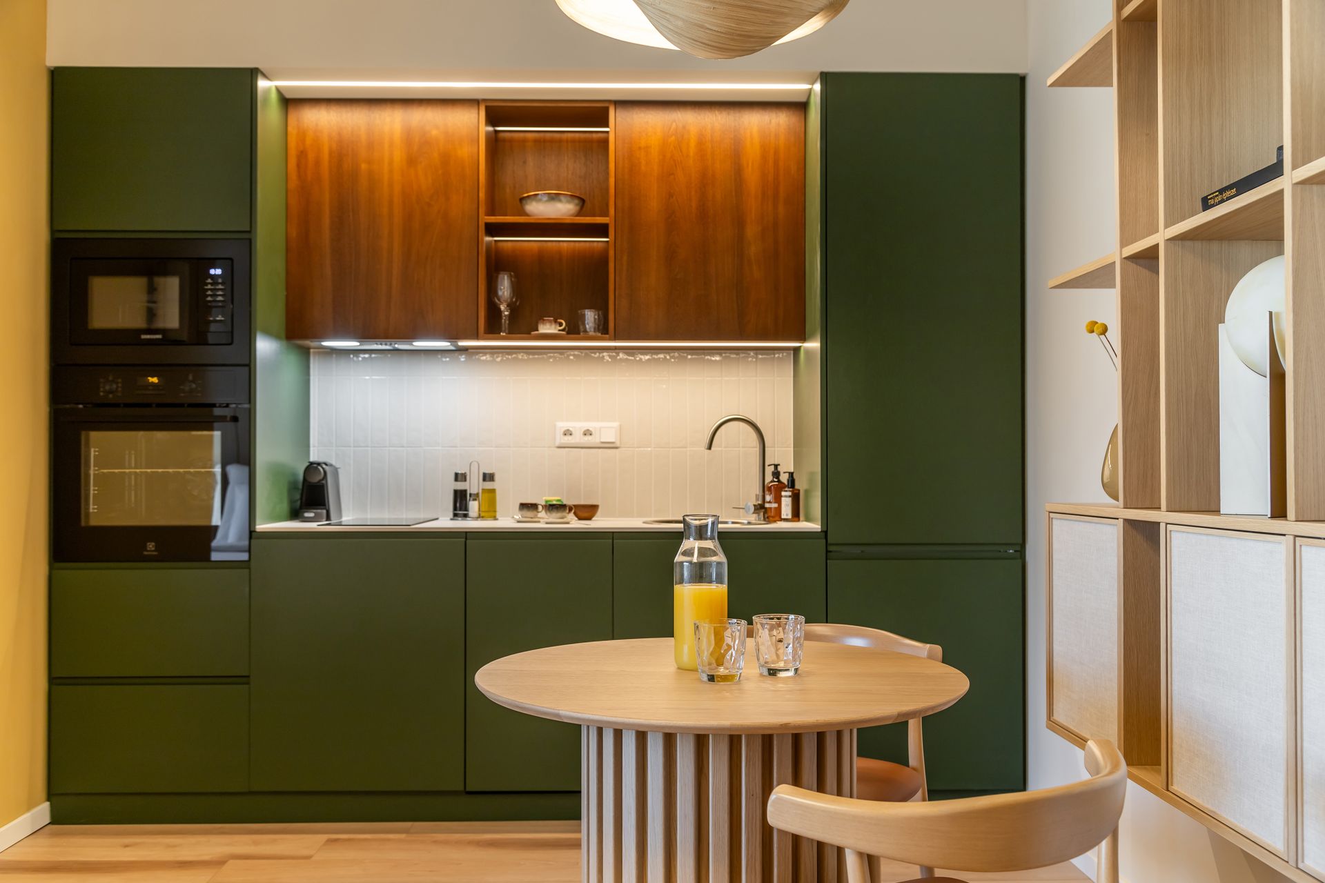 Modern kitchen with green cabinets, wooden upper cabinets, and a round wooden table in Marone Suites Budapest.